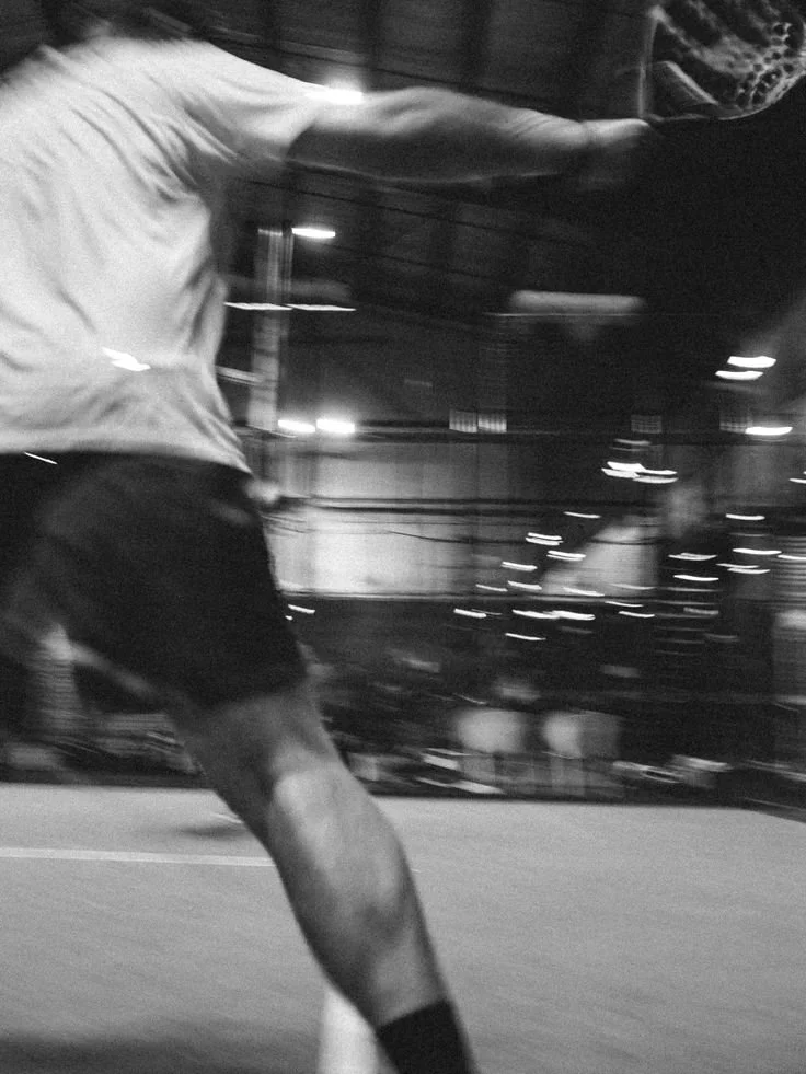 A black and white photograph of a person in sports gear, captured mid-motion, possibly playing soccer or football indoors.