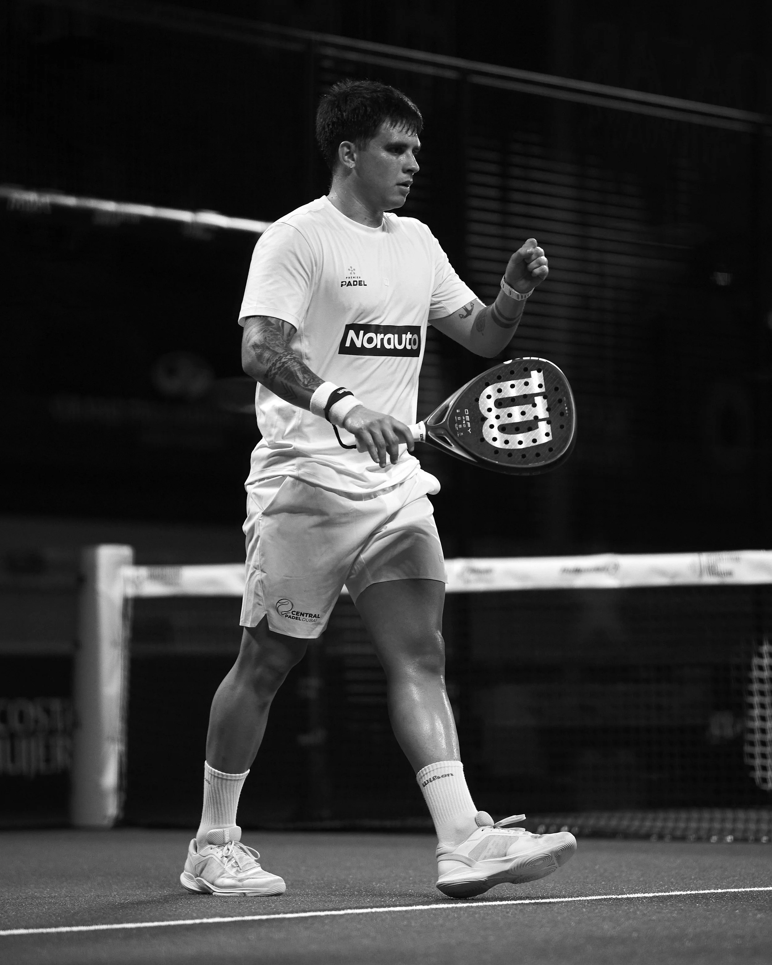 A male padel player dressed in sportswear, holding a padel racket, on an indoor court, with a focused expression.