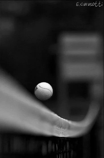 Close-up of a golf ball on a tee with a golf club about to strike it, black and white photo.