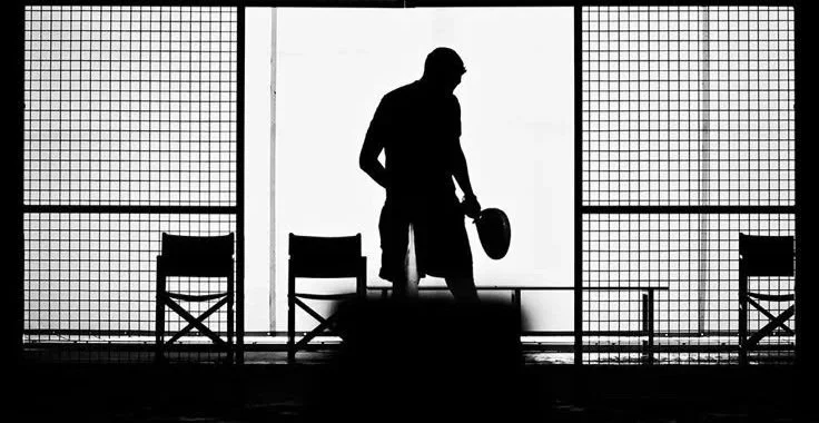 Silhouette of a person holding a helmet, standing between two chairs on a stage with a grid-patterned background.