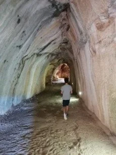 Personne marchant dans une grotte avec des parois rocheuses colorées et une surface d'eau au sol