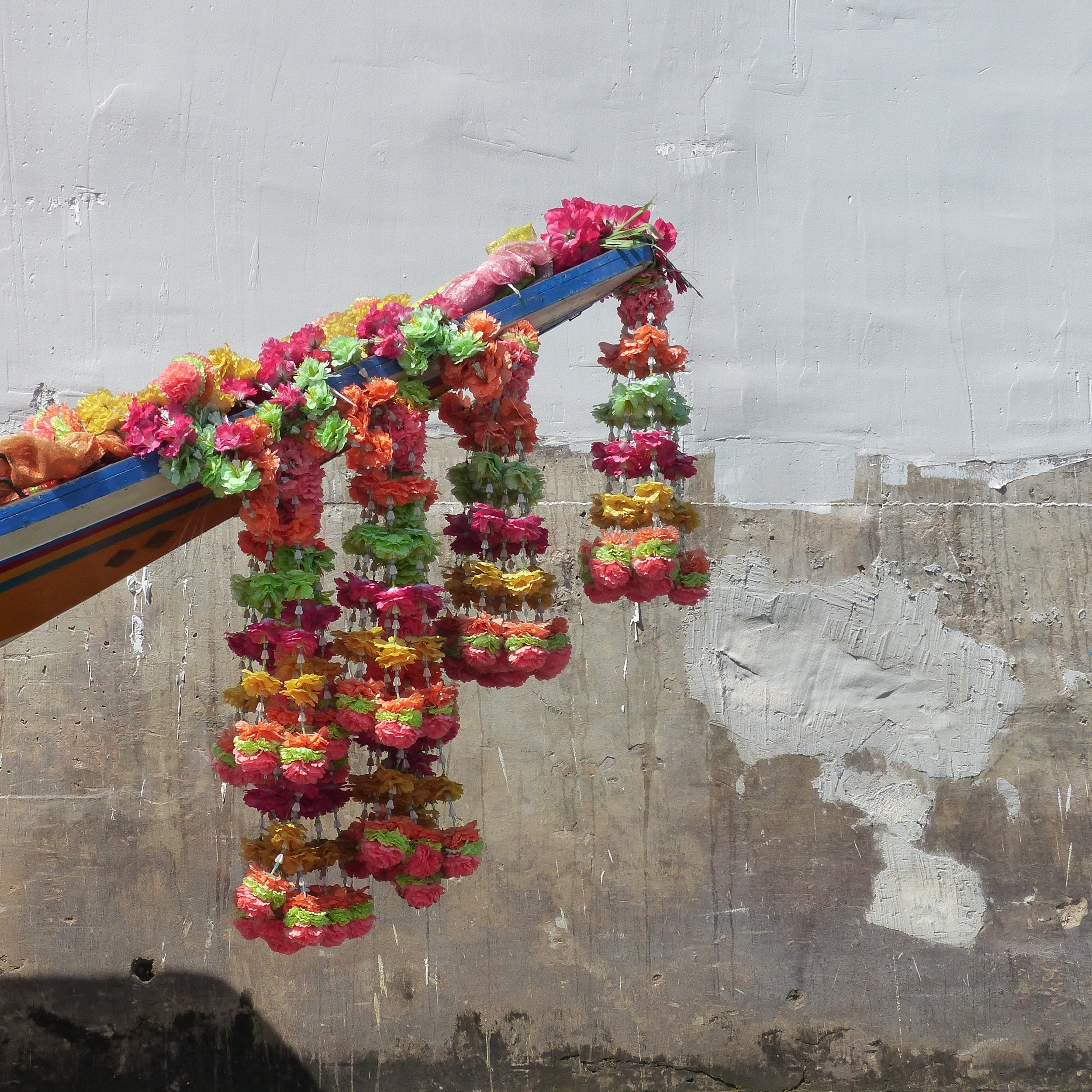 Flores de papel de colores colgadas en forma de escalinata frente a una pared gris.