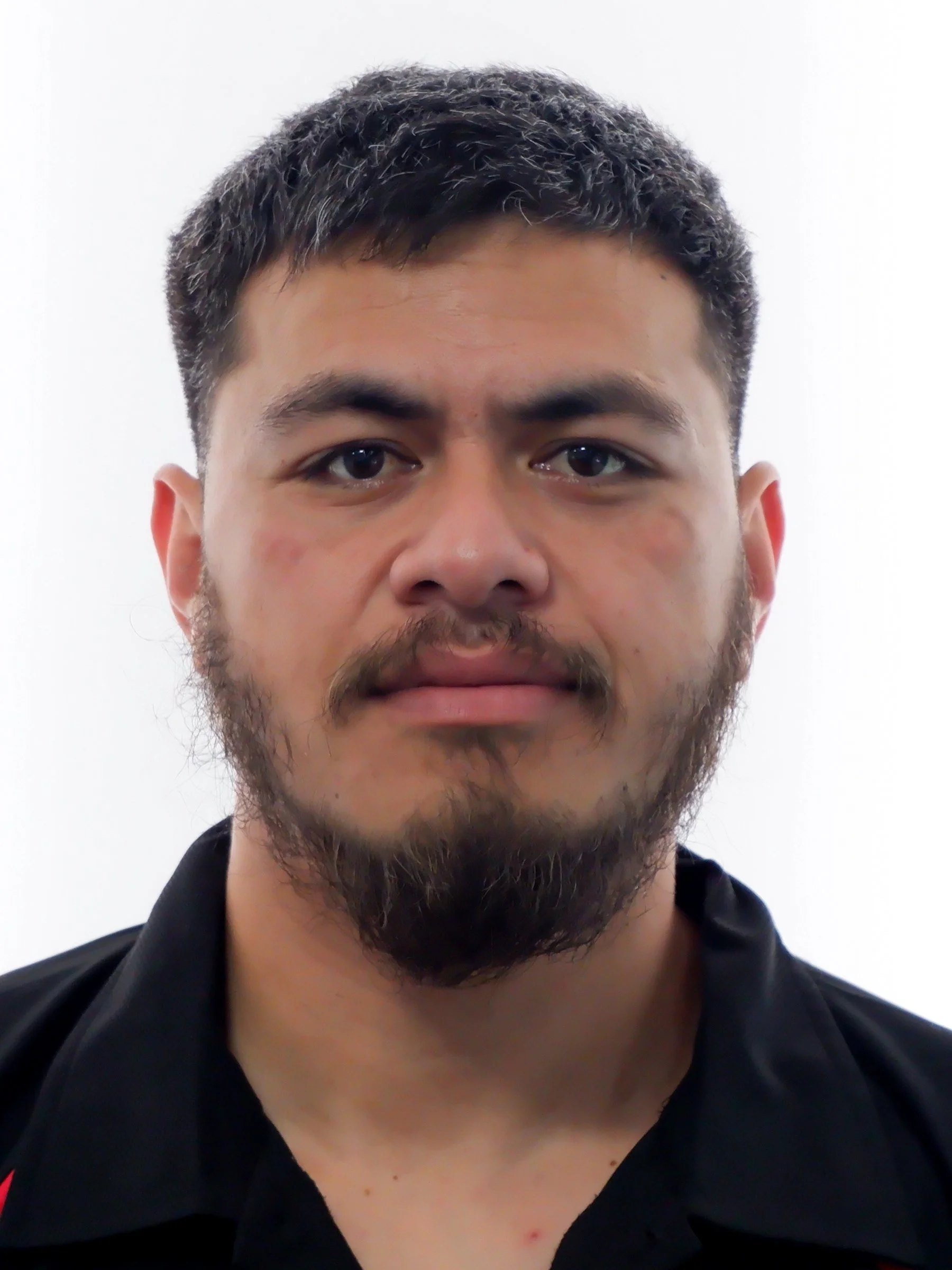 Close-up of a man with short dark hair and a beard, wearing a black shirt, against a white background.