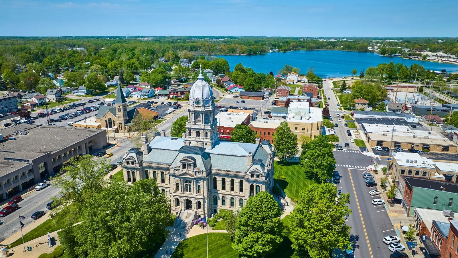 Aerial view of a small town with a historic courthouse, a church, and a lake in the background.