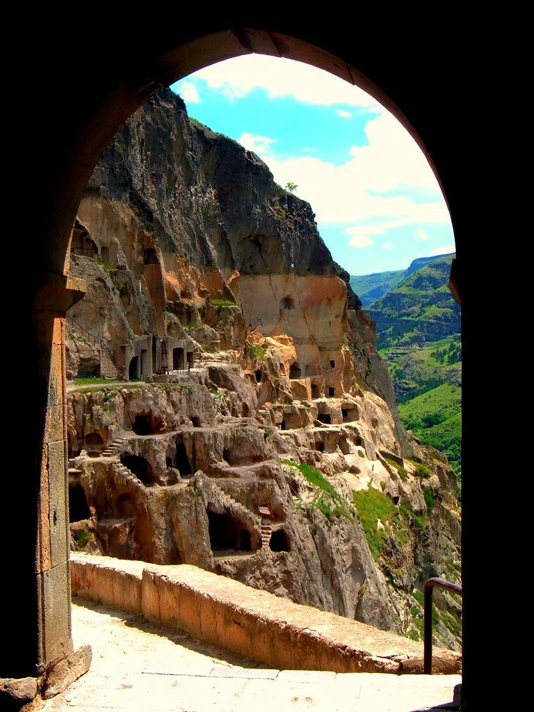 Ancient cave dwellings built into a mountainside viewed from an arched tunnel.