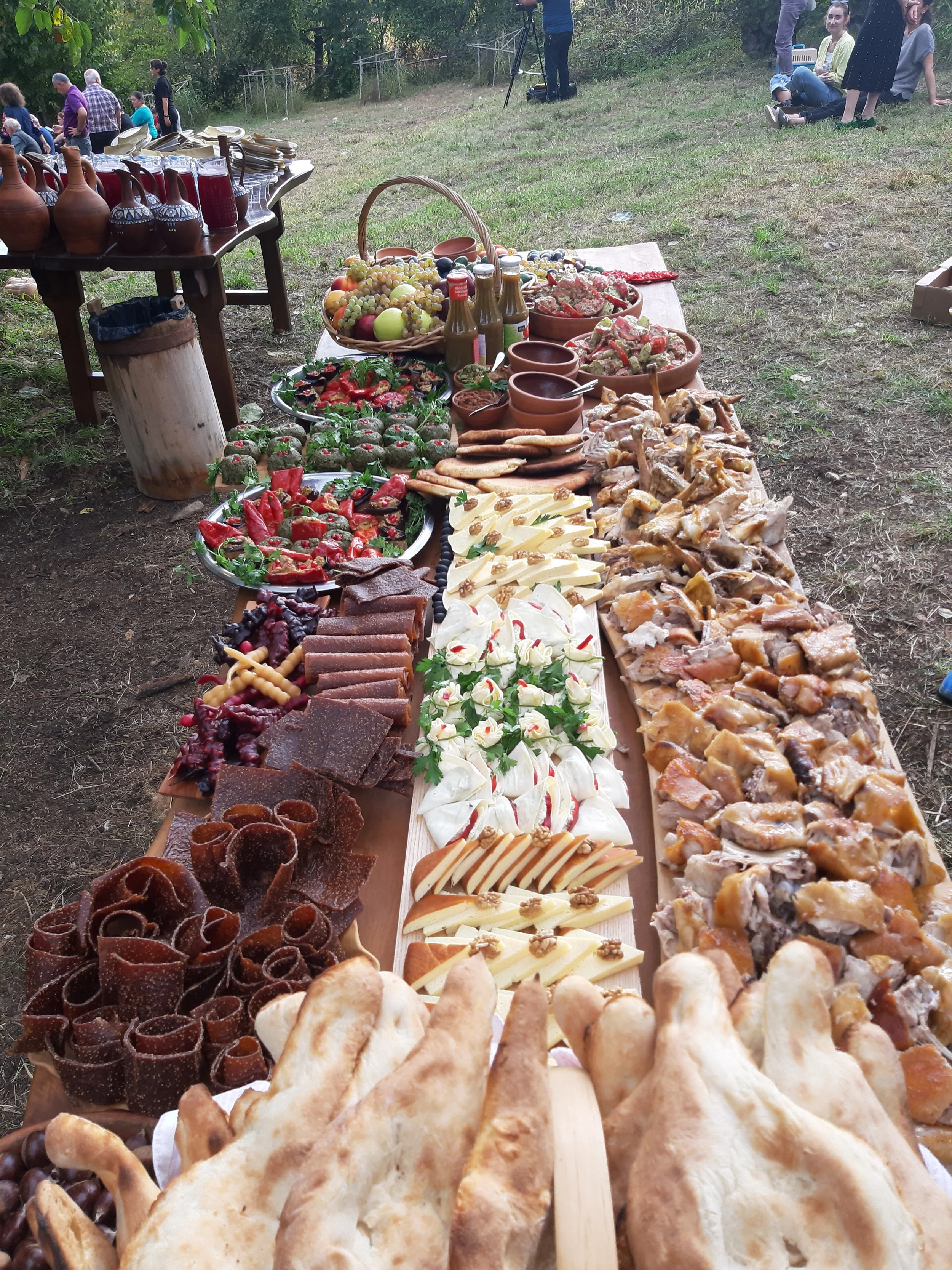 Table filled with various foods and desserts at an outdoor event, with people in the background.