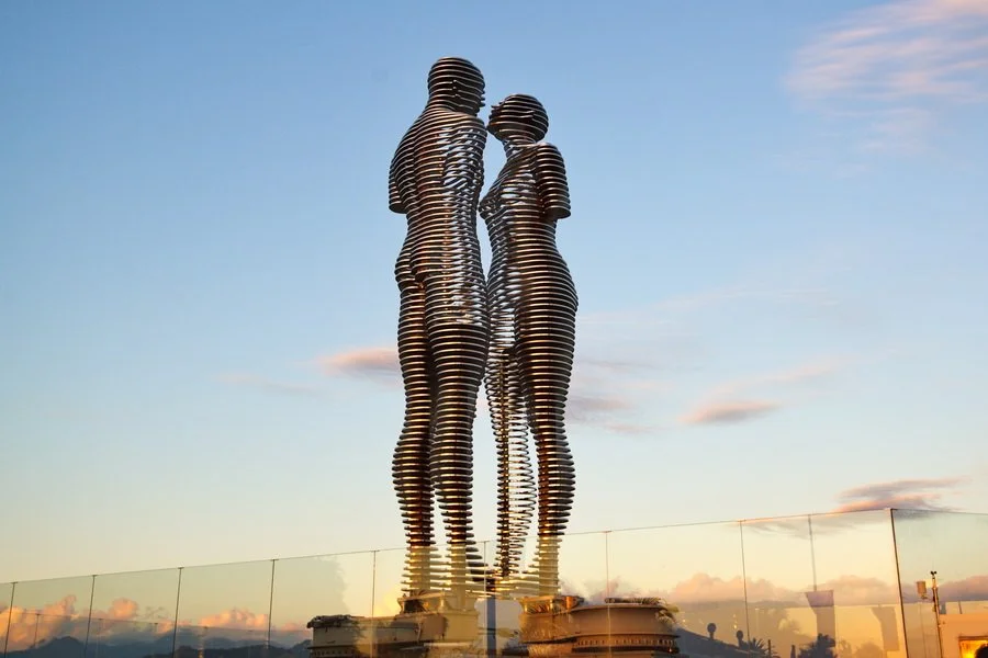An architectural sculpture of a man and woman facing each other on a rooftop, made of horizontal metal rings.