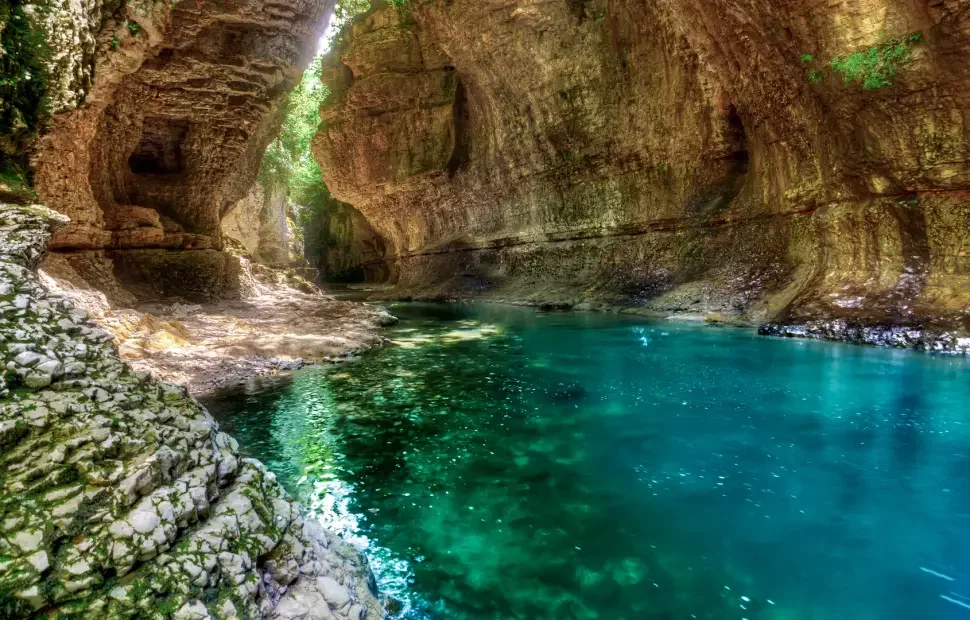 A scenic stream flowing through a rocky canyon with steep, moss-covered walls and lush green vegetation.