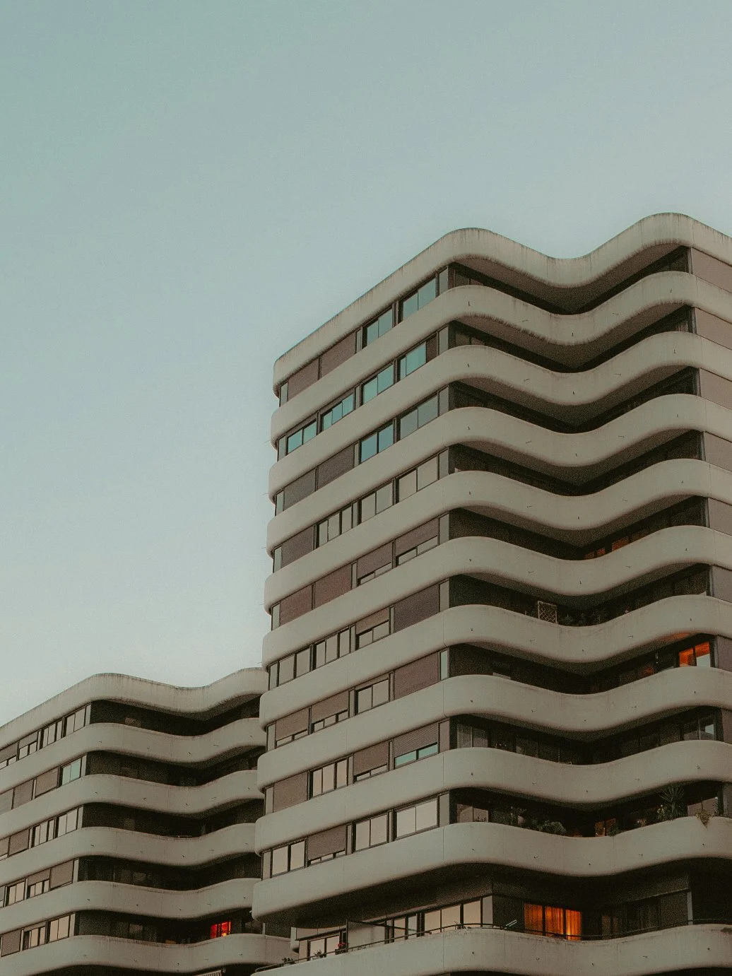Un immeuble moderne avec des balcons ondulés et de nombreuses fenêtres, photo prise en fin de journée.