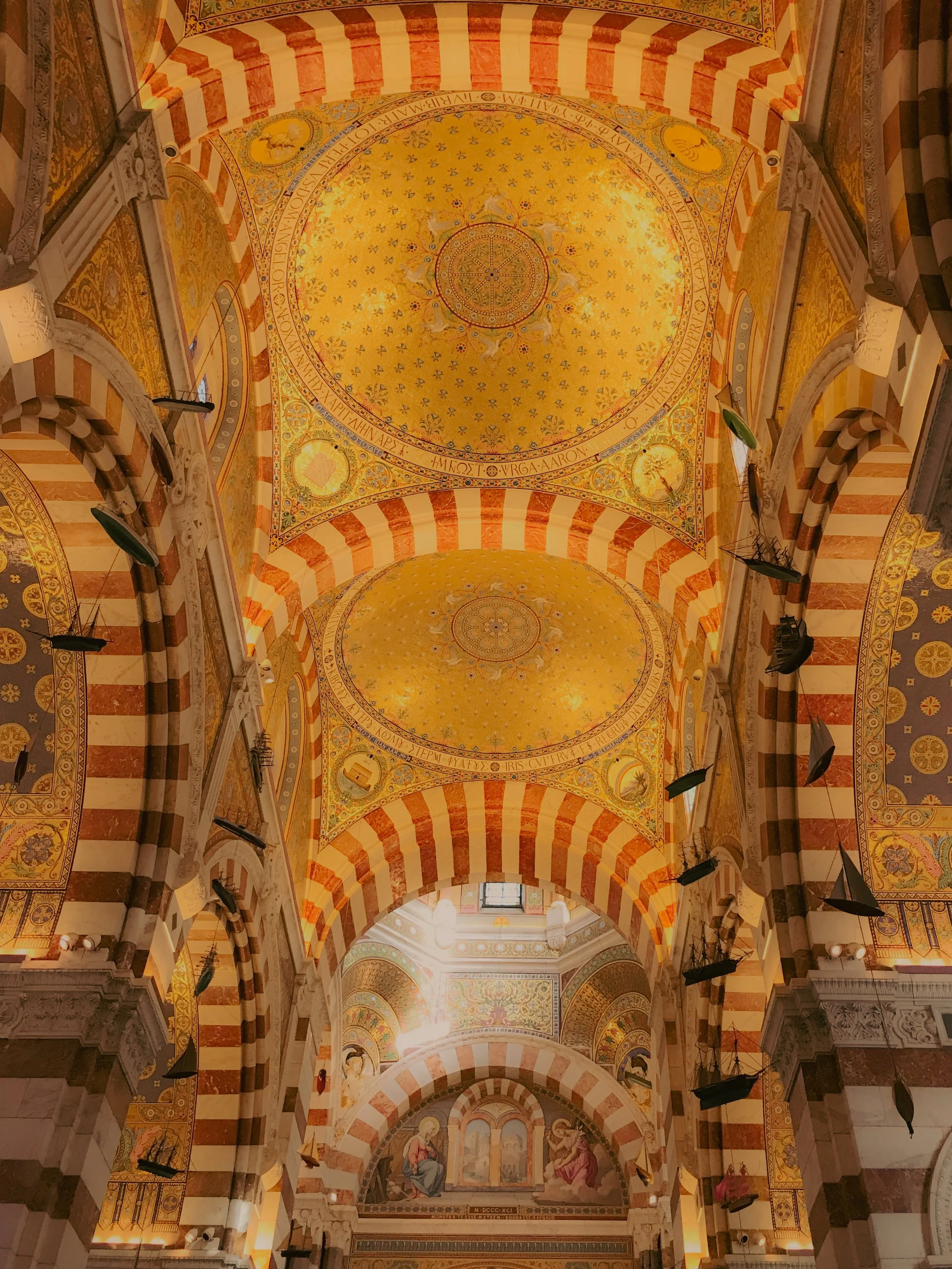 Plafond décoré avec des motifs dorés et des étoiles dans une architecture religieuse, avec des arches en brique rouge et blanche, et des fresques au fond représentant des figures religieuses.