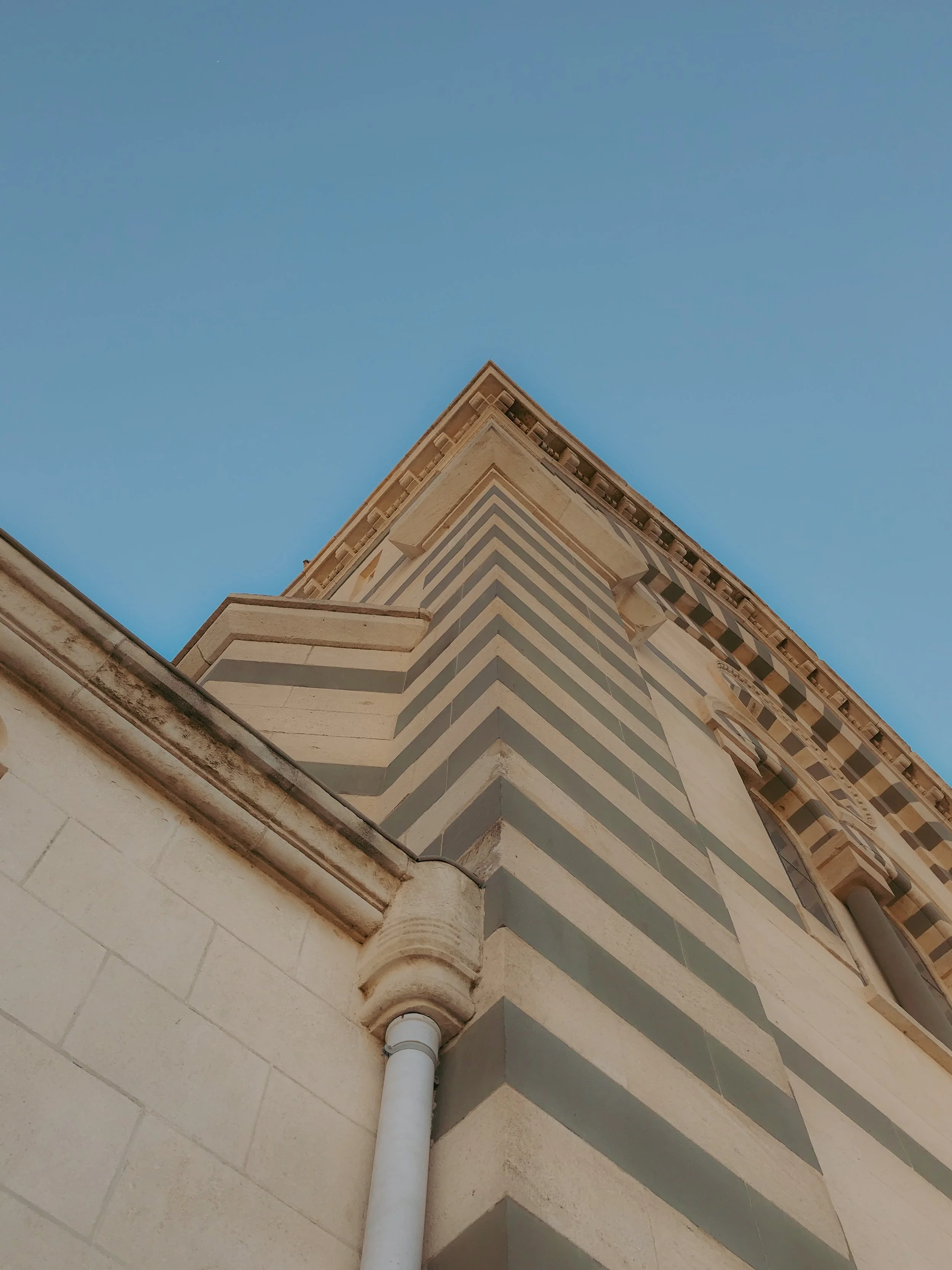 Vue en contre-plongée d'un bâtiment à rayures horizontales beige et vert foncé, avec un ciel bleu en arrière-plan.