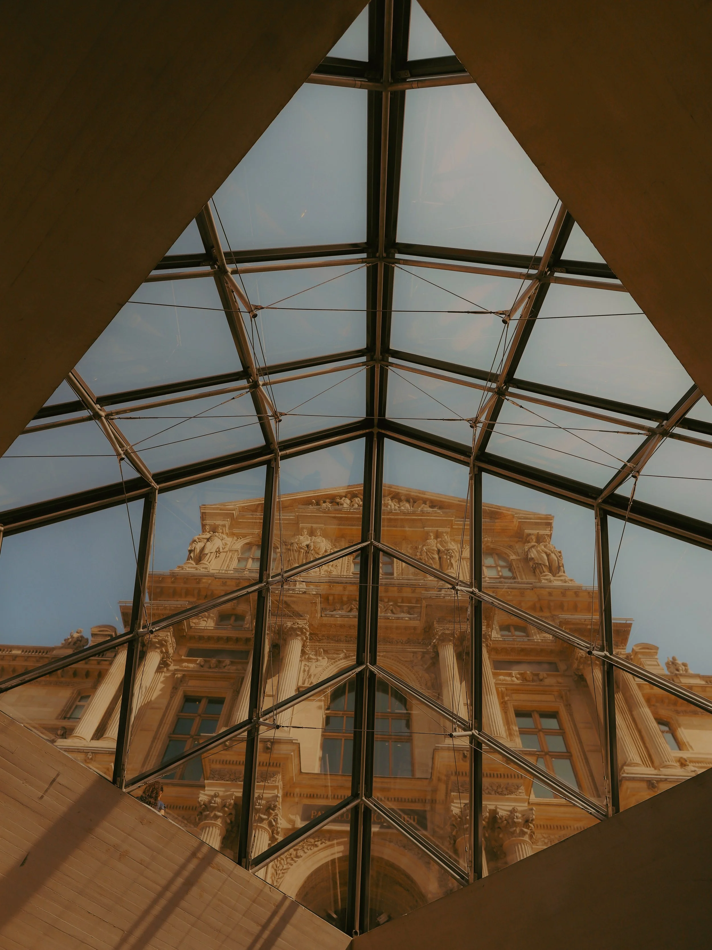 Vue à travers un plafond de verre montrant une architecture ancienne en façade, avec des colonnes et des sculptures.