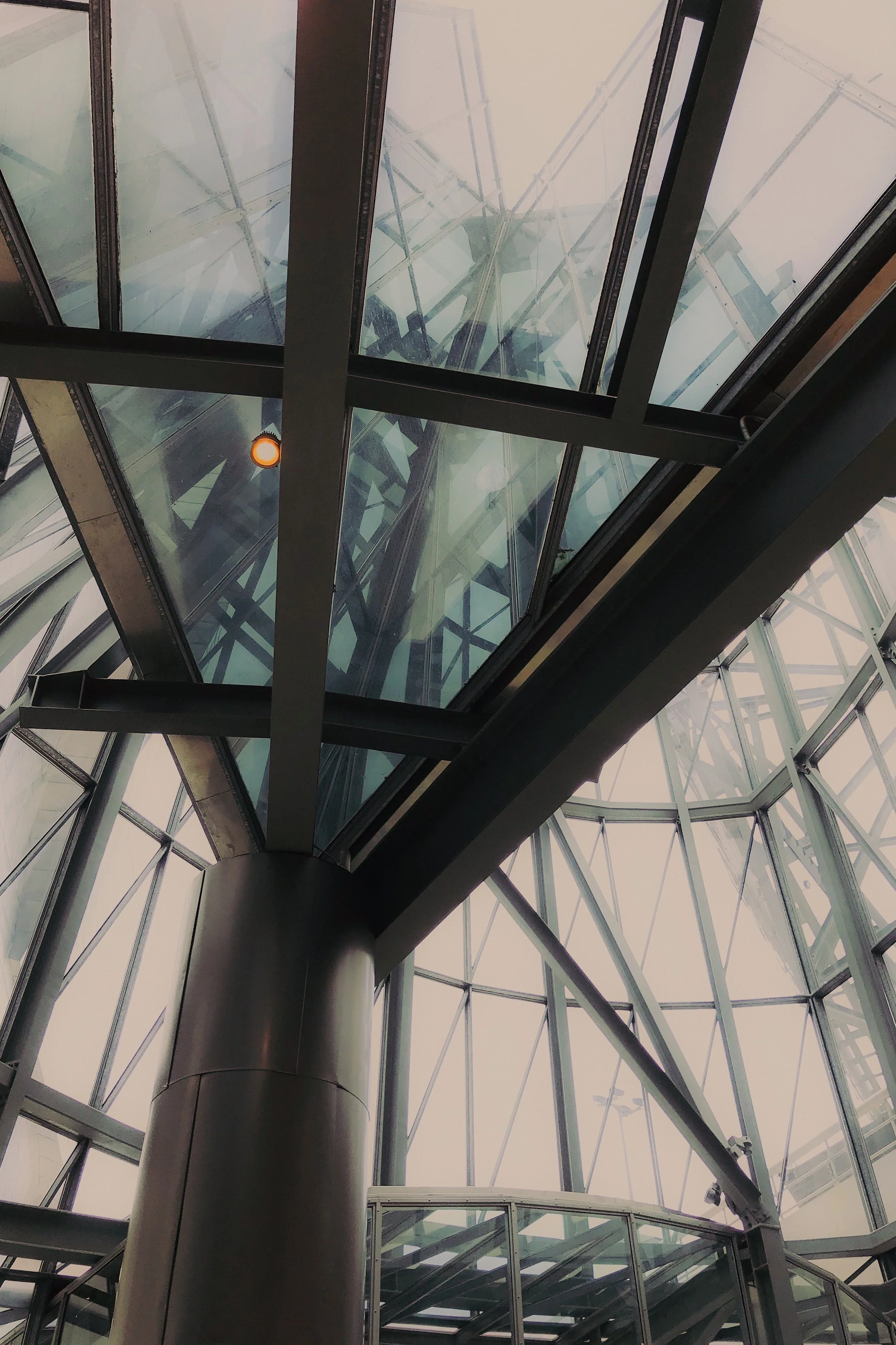 Vue en contre-plongée d'une structure en métal et en verre, incluant un ascenseur ou un tunnel de transport suspendu au plafond.