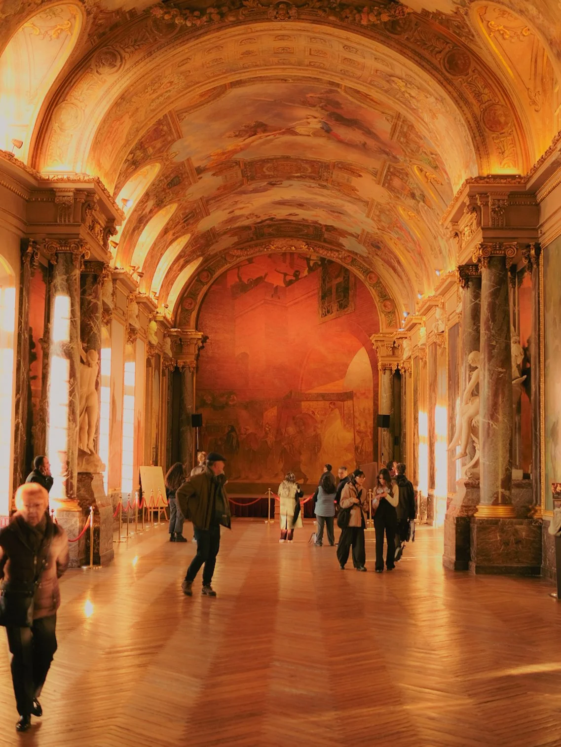 Une salle de musée avec des murs ornés de fresques et de sculptures, des colonnes en marbre, et plusieurs visiteurs.