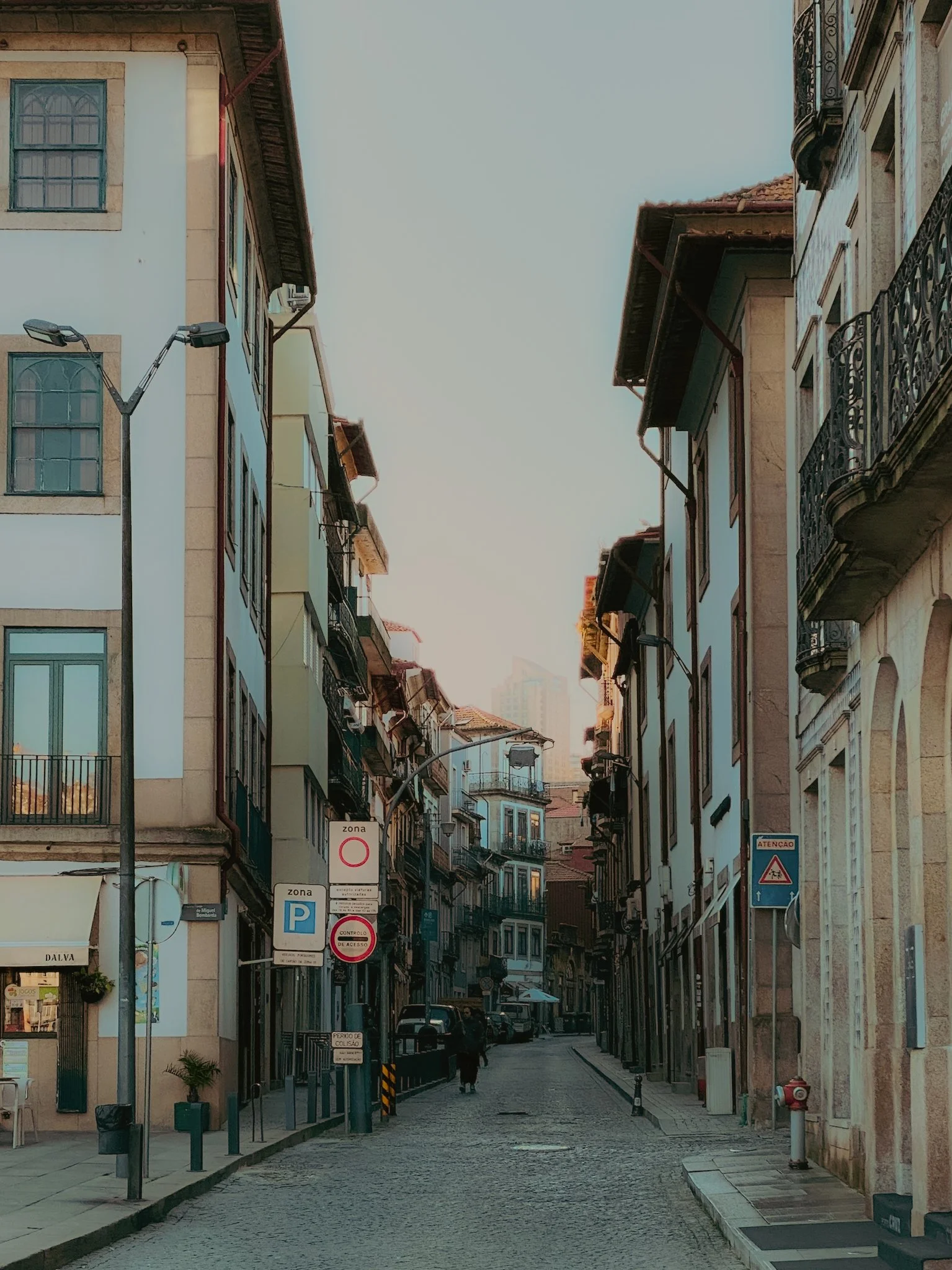 Rue pavée bordée de bâtiments anciens avec des balcons en fer forgé, lampadaires et panneaux de signalisation, dans une ville européenne.