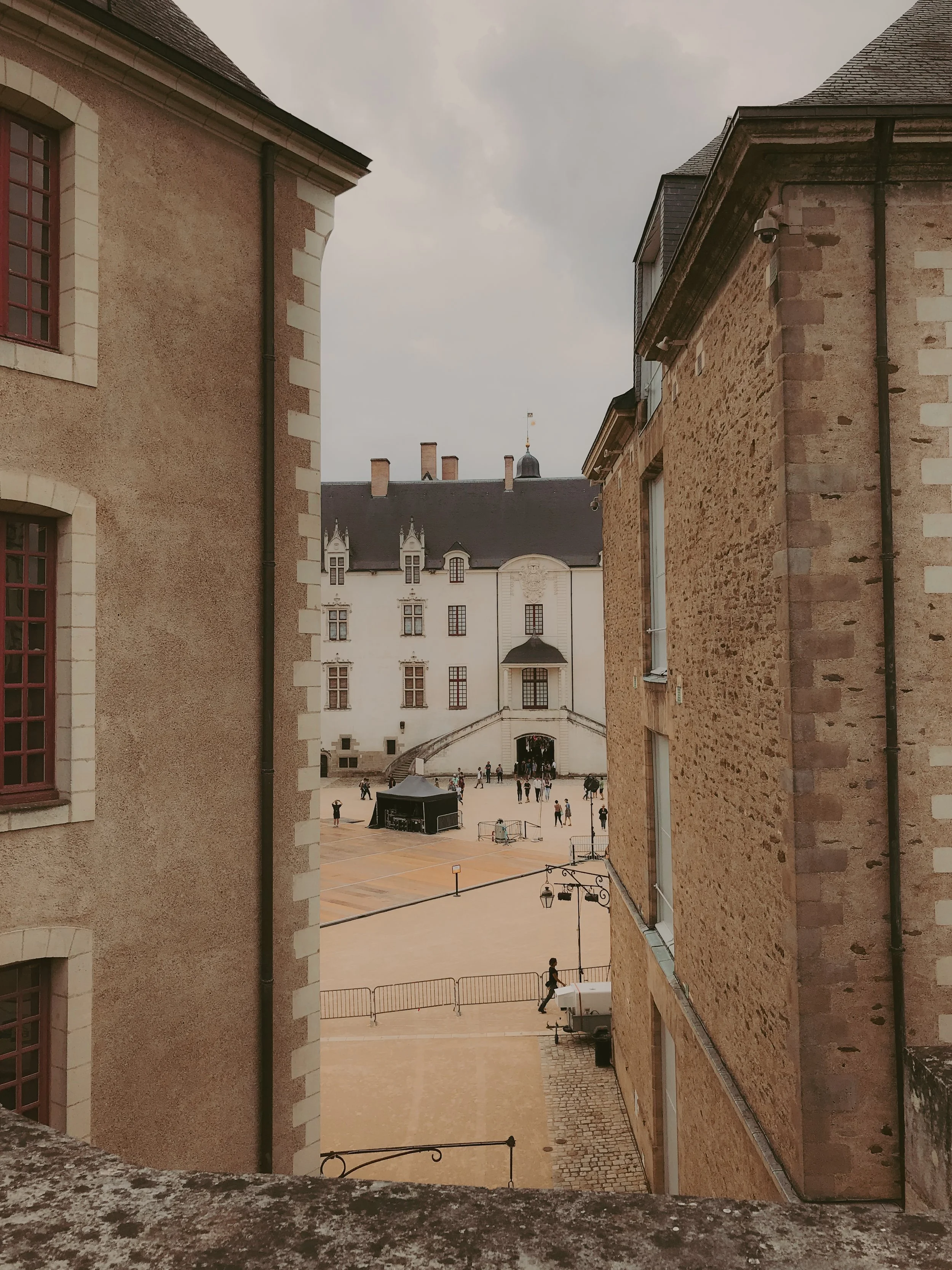 Une vue d'un bâtiment historique blanc vu entre deux bâtiments en pierre, avec une cour et des gens qui se promènent.