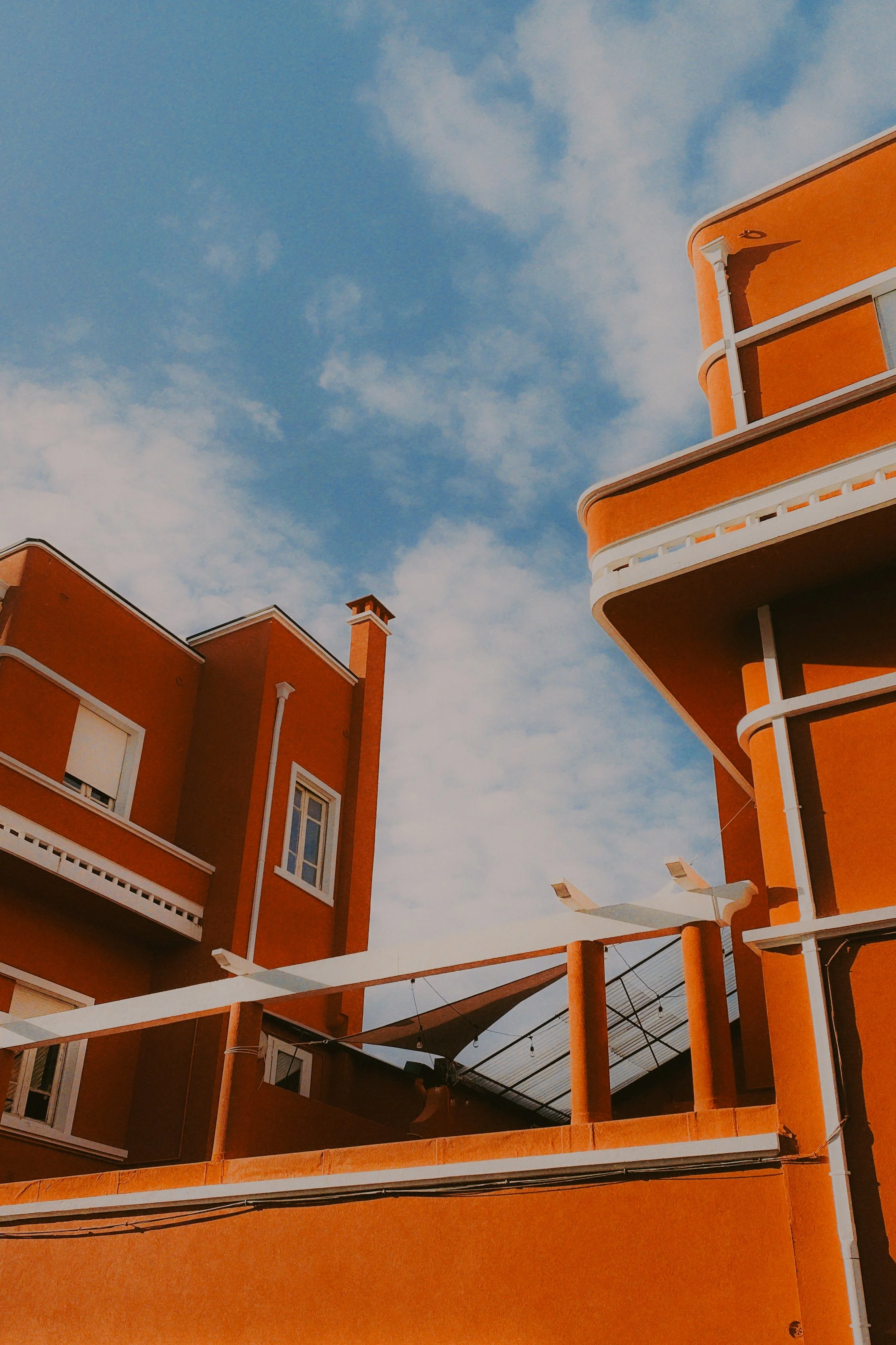 Bâtiments en architecture moderne de couleur orange avec balcons et fenêtres, et un ciel bleu avec quelques nuages.