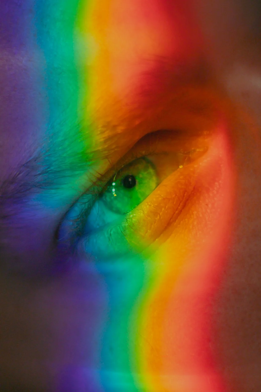 Zoom sur un œil humain avec une lumière colorée en arc-en-ciel reflétée, accentuant le regard et les détails de la peau autour de l'œil.