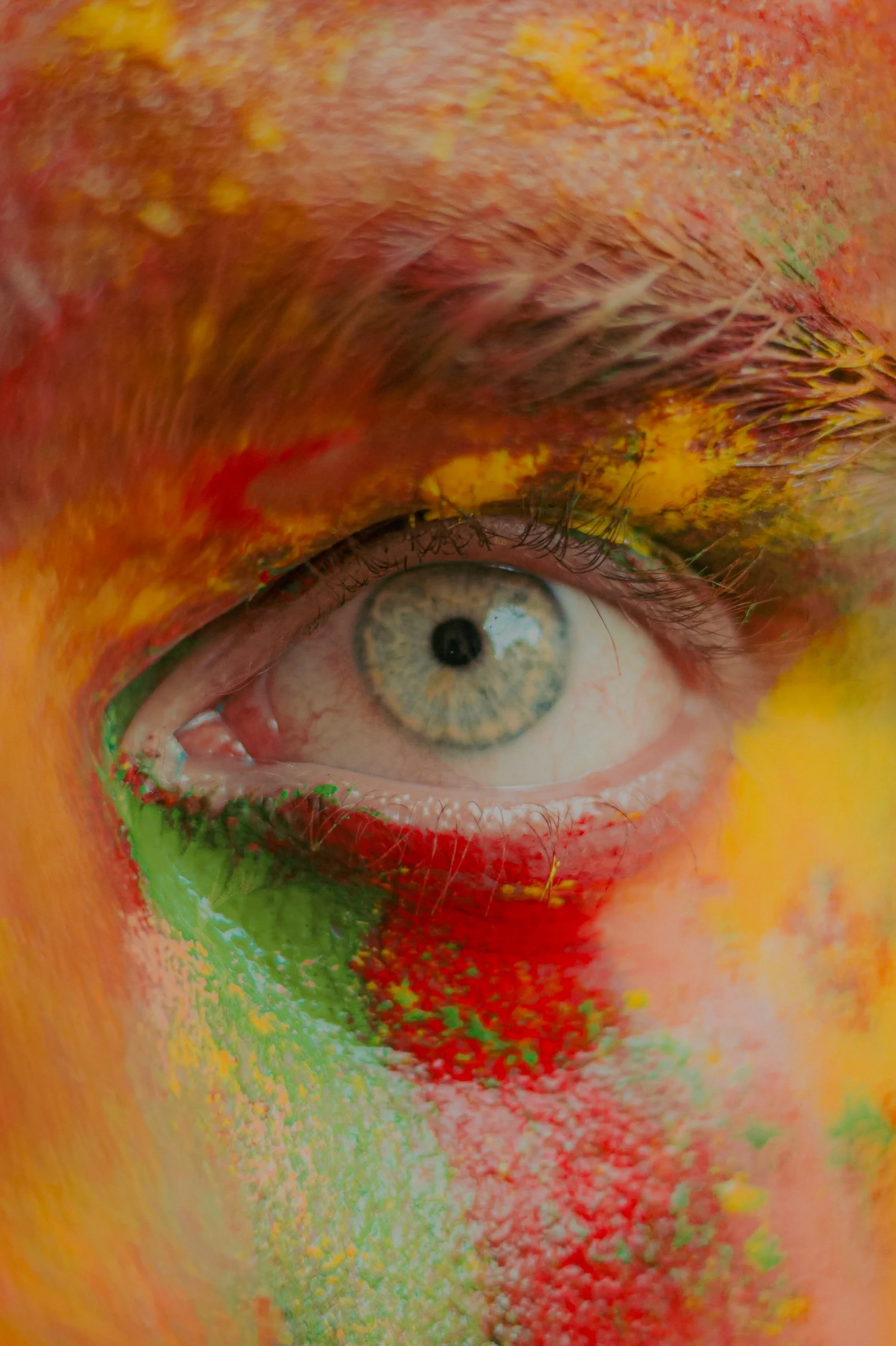 Un œil humain entouré de peintures colorées en rouge, vert, jaune et orange.
