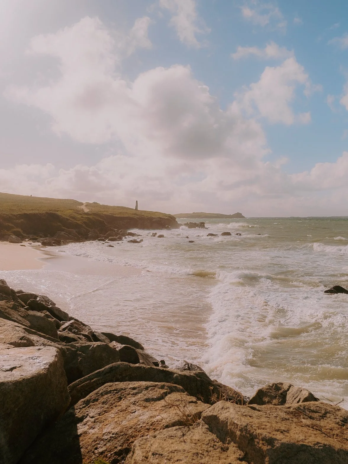 Côte rocheuse avec la mer, vagues et ciel partiellement nuageux.