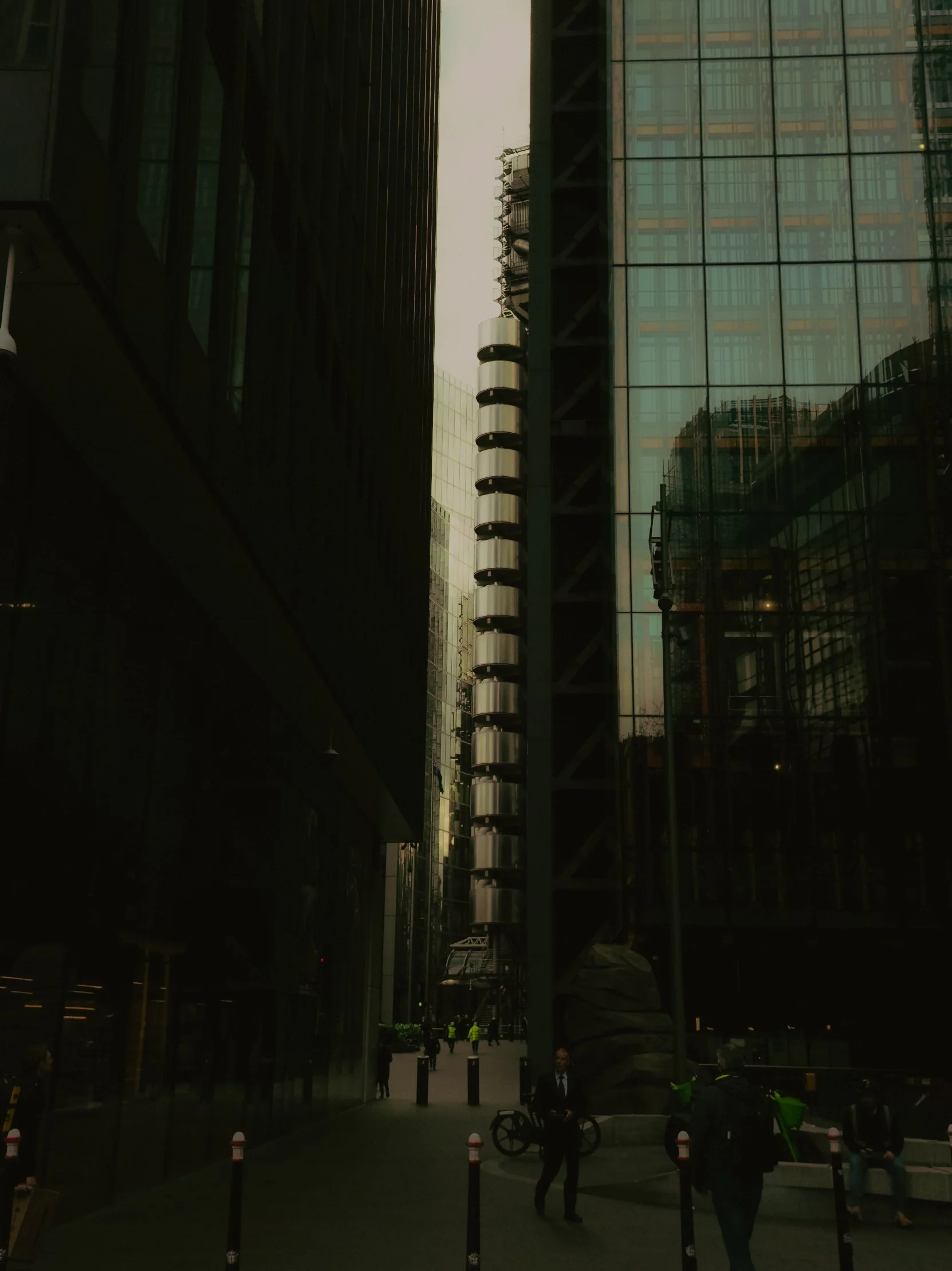Une rue urbaine entourée de gratte-ciel en verre, avec des passants et des employés en costume, un vélo et une sculpture en pierre au centre.