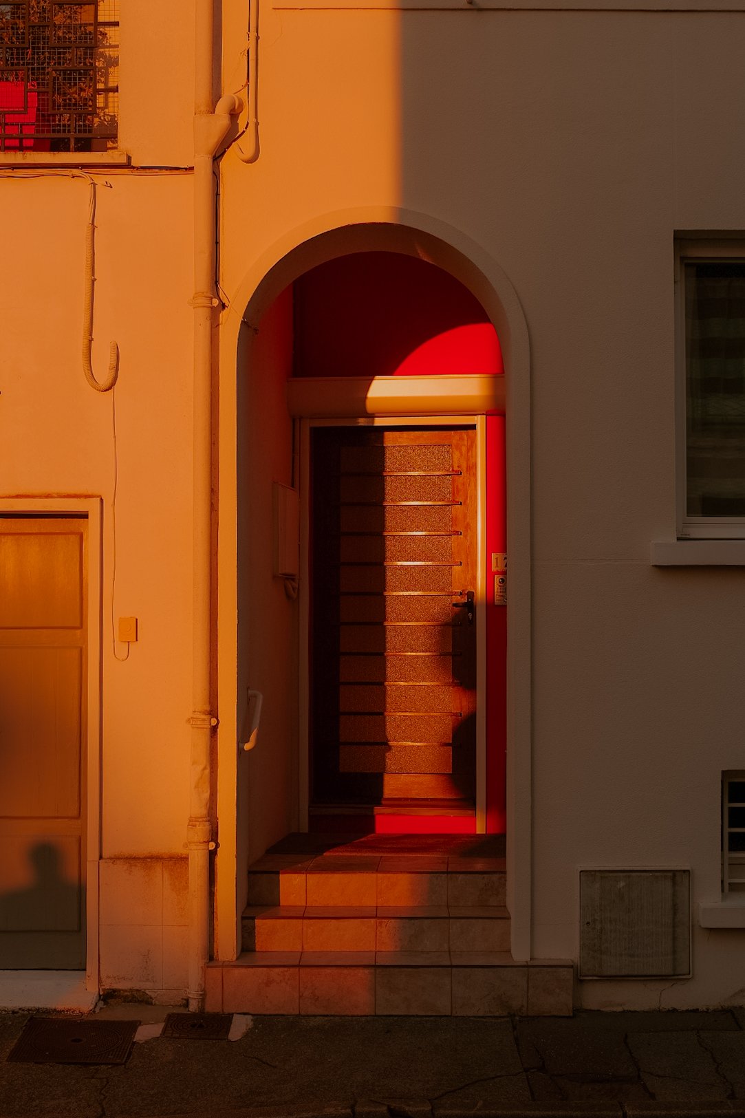 Une porte d'entrée encadrée d'un arc, avec un escalier menant à la porte, sous la lumière chaude du coucher du soleil.