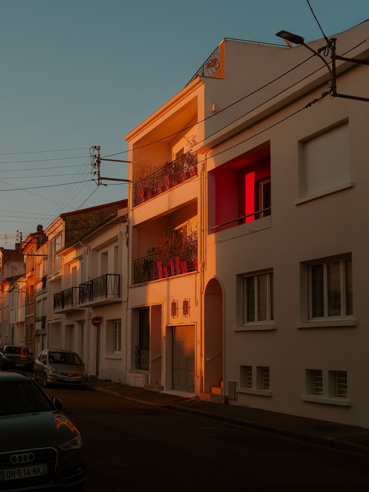 Immeubles résidentiels sous la lumière du coucher du soleil, avec voitures stationnées sur la rue.