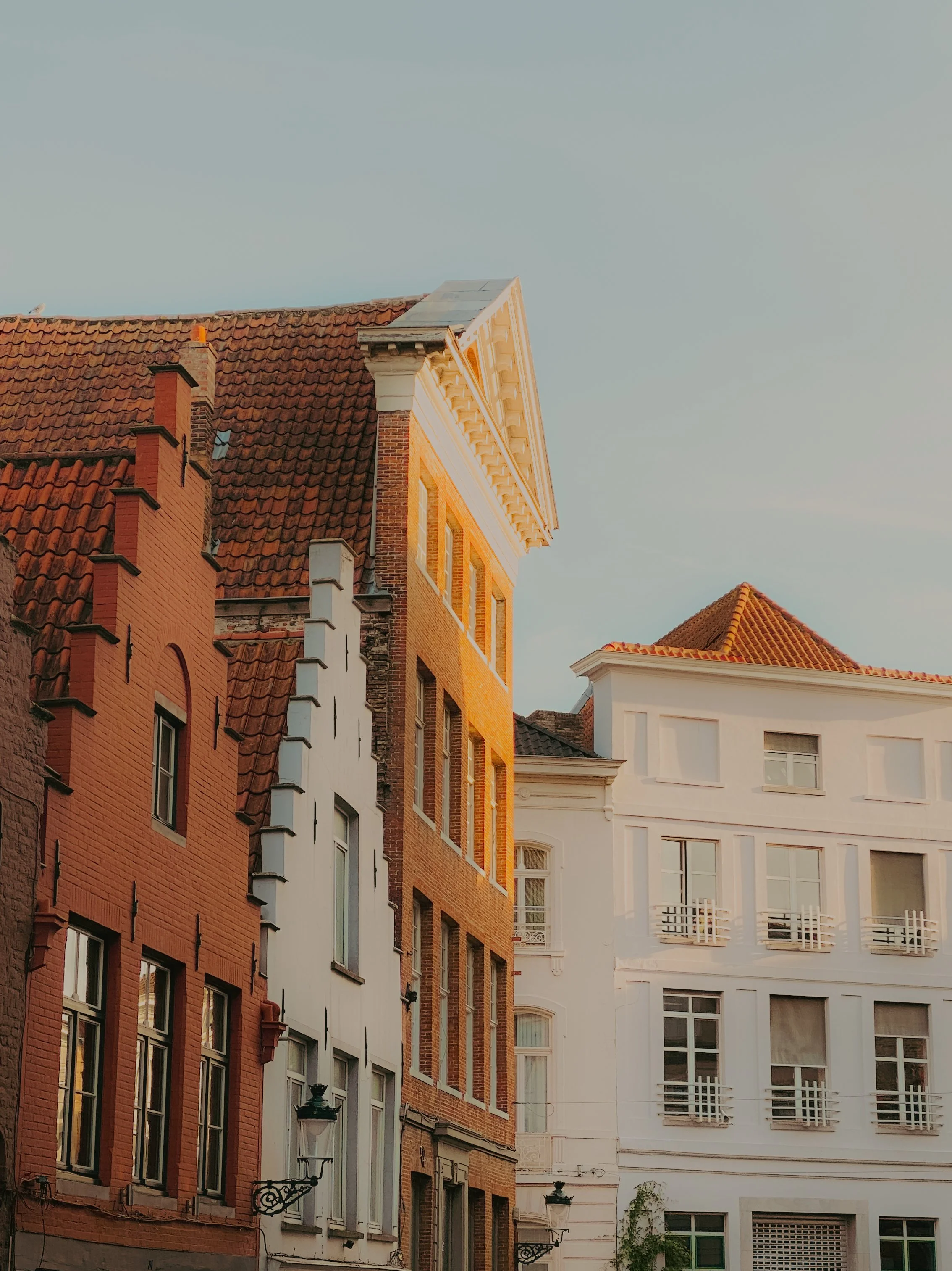 Vue de bâtiments résidentiels avec des façades en brique et en blanc, toits en tuiles rouges, sous un ciel clair, en fin d'après-midi.