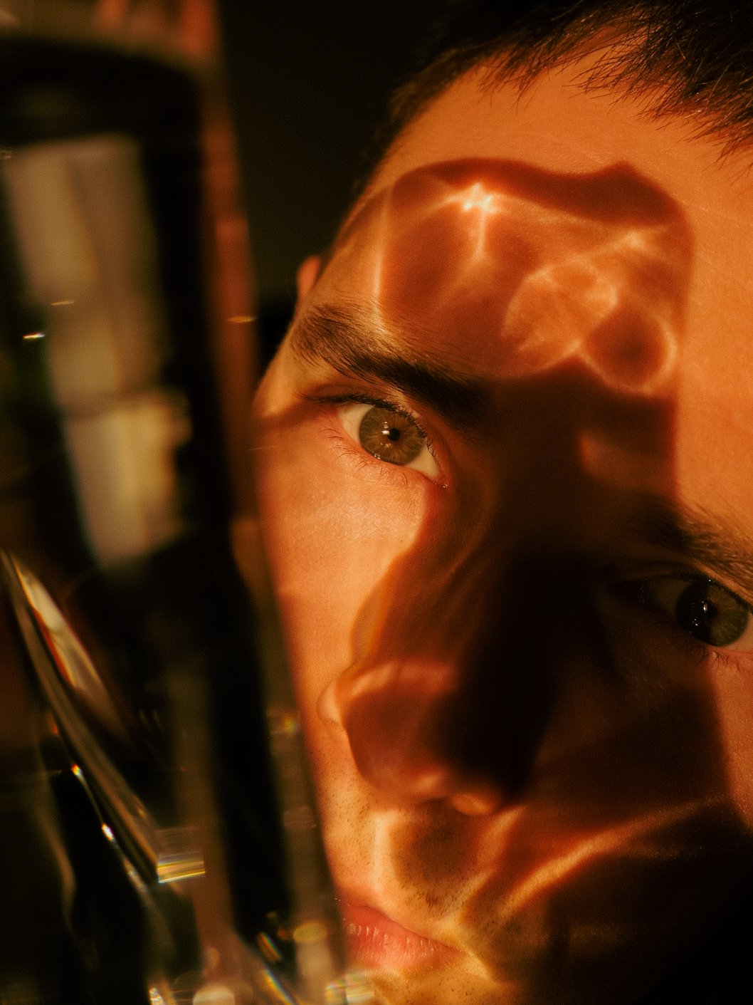 Un jeune homme regarde à travers une lentille, avec un jeu de lumière et d'ombres sur son visage et ses yeux ainsi que la lentille.