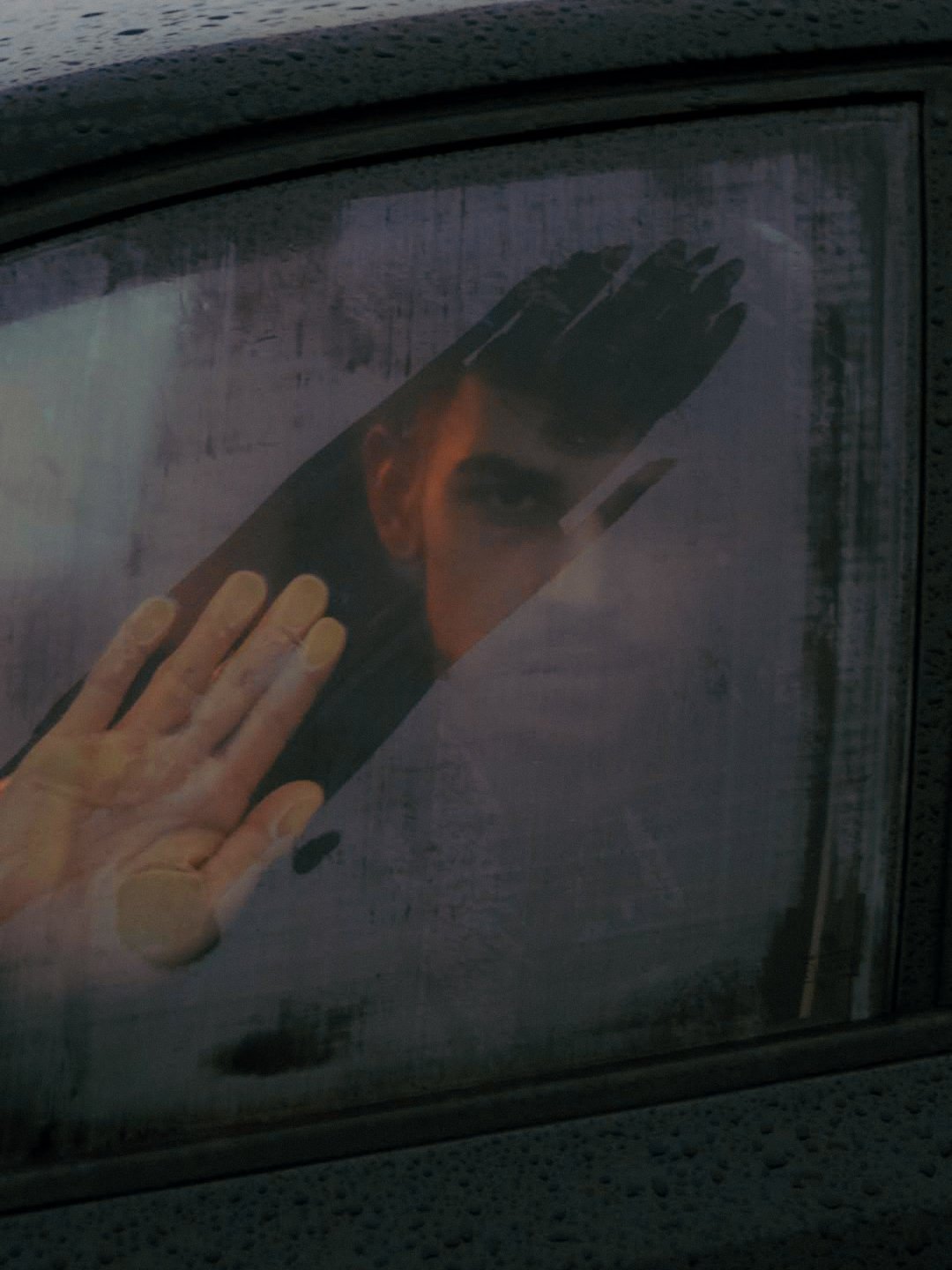 Sticker sur une voiture représentant un visage d'une personne avec des cheveux noirs, regardant vers l'avant. La main d'une personne appuie sur le sticker.