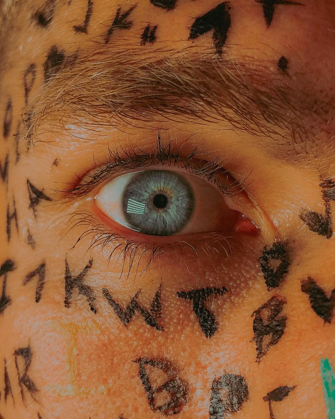 Un œil humain avec une pupille bleue et iris gris, entouré de tatouages en noir.