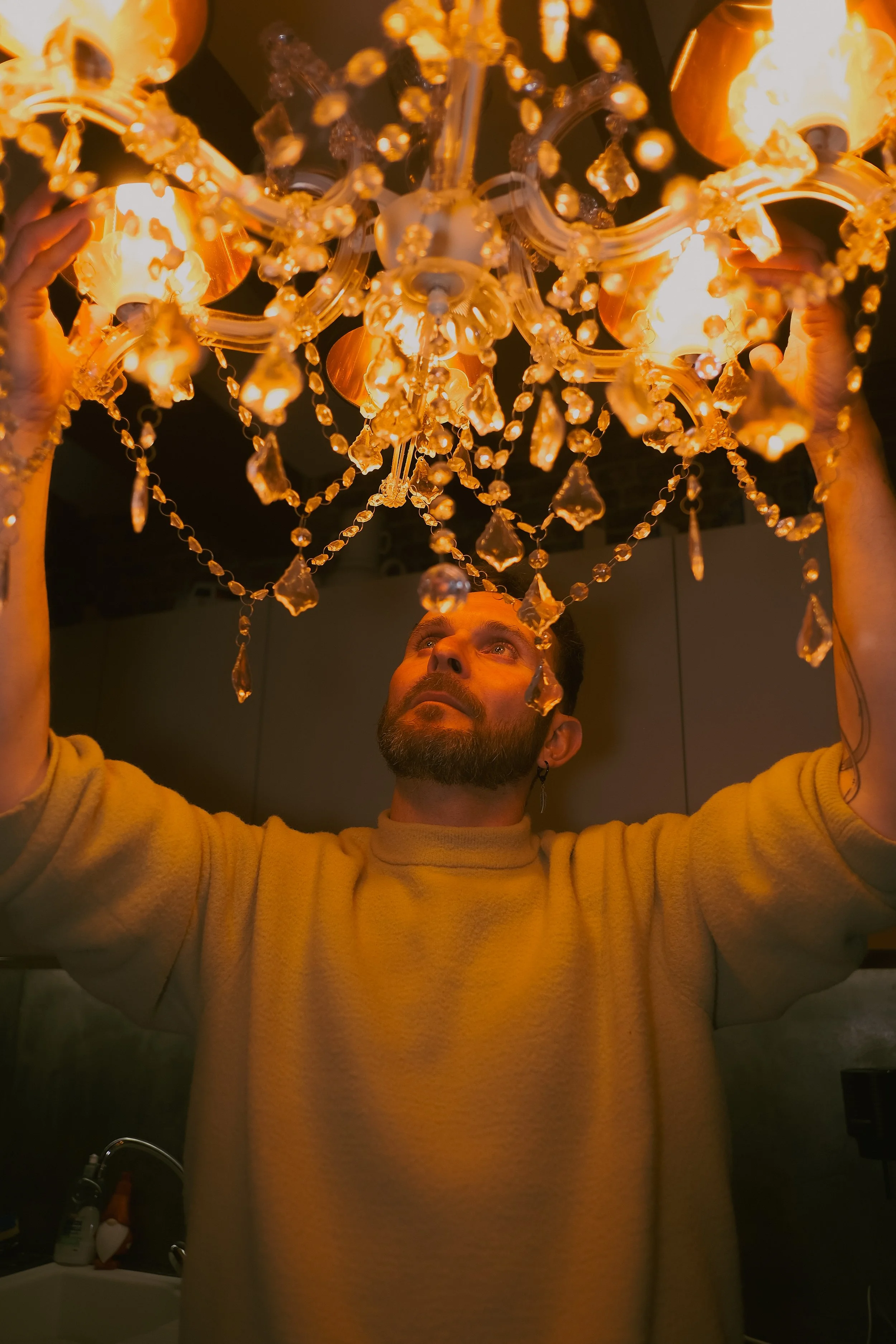 Homme ajustant un lustre en cristal dans une pièce sombre.