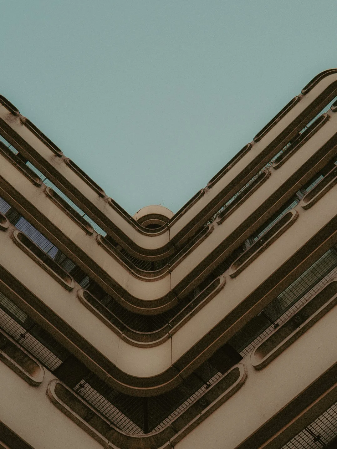 Vue en contre-plongée d'un bâtiment résidentiel avec plusieurs étages et balcons en forme de courbe, vu du bas vers le haut avec ciel clair en arrière-plan.