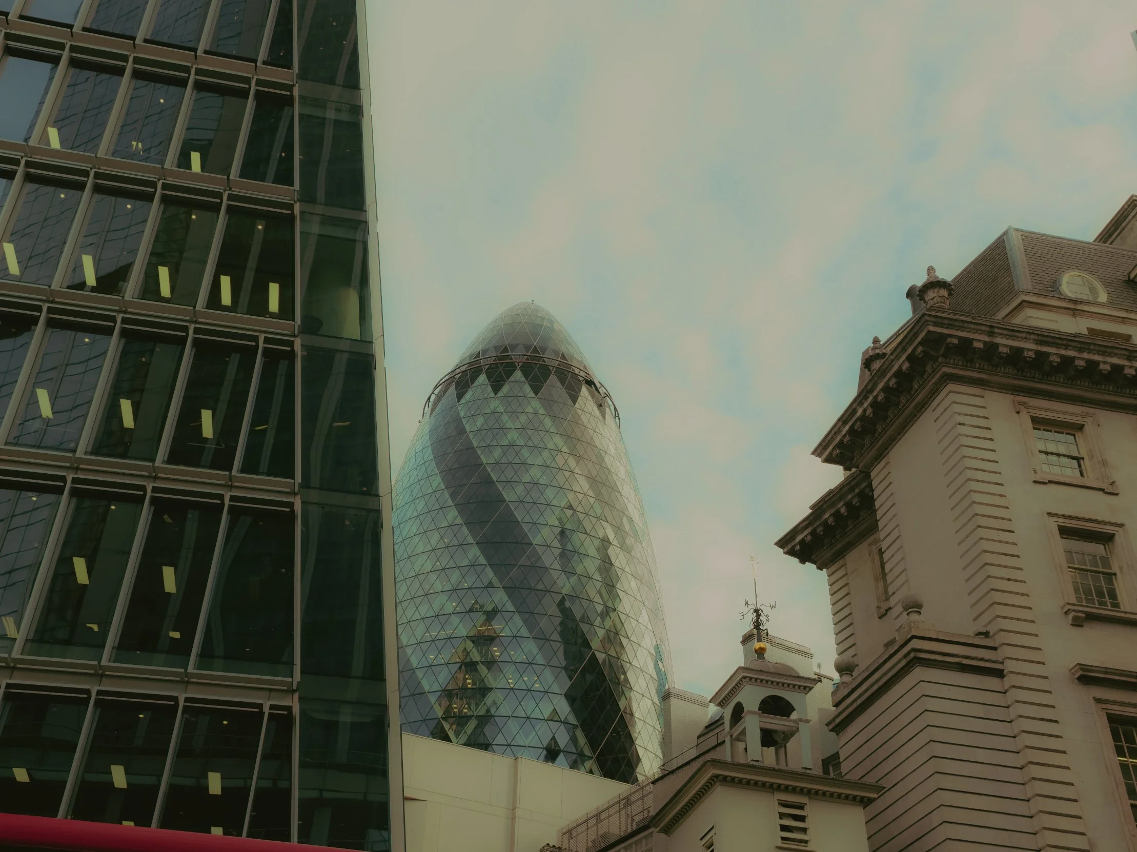 Photo de plusieurs bâtiments modernes et anciens dans un centre-ville, avec un ciel nuageux en arrière-plan.