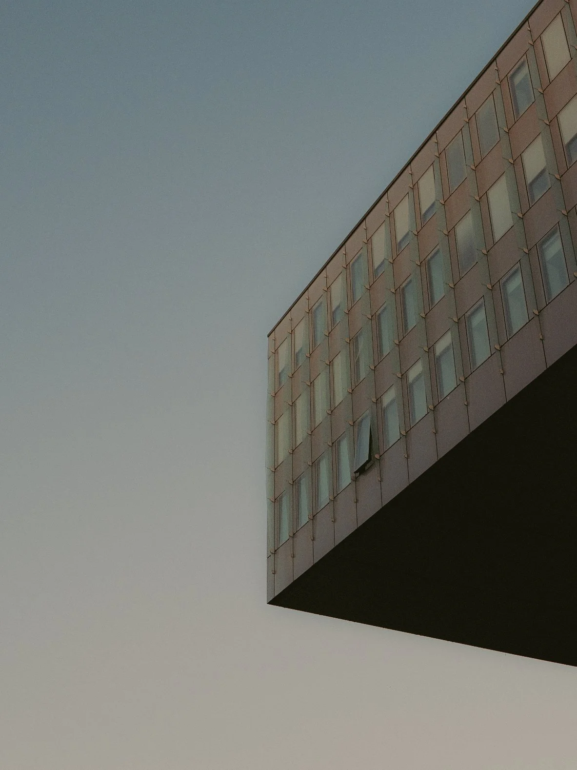 Vue en perspective d'un bâtiment moderne avec une façade en verre et un ciel clair.