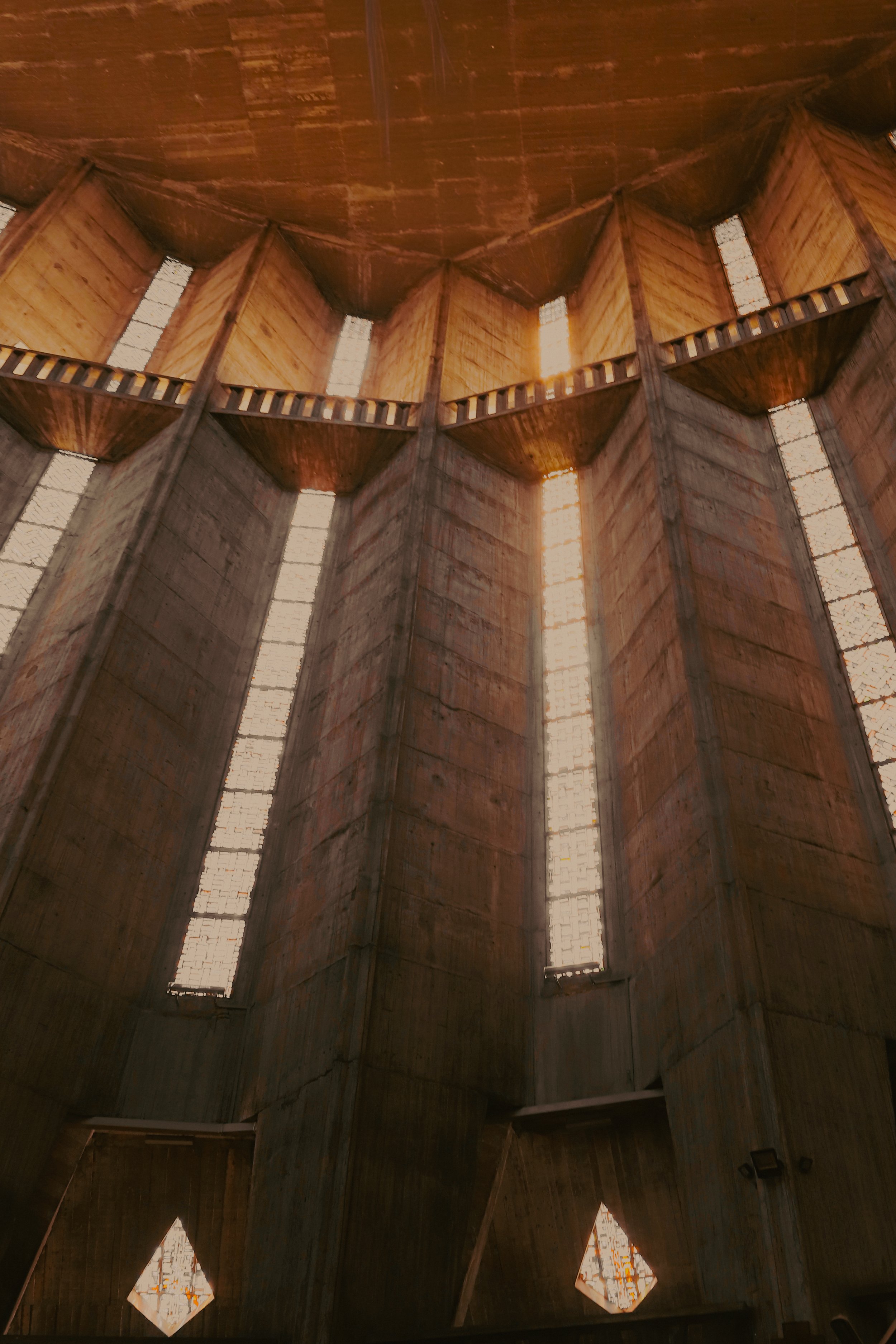 Intérieur d'une église ou d'une structure en béton avec de hautes fenêtres verticales laissant passer la lumière, vue en contre-plongée.