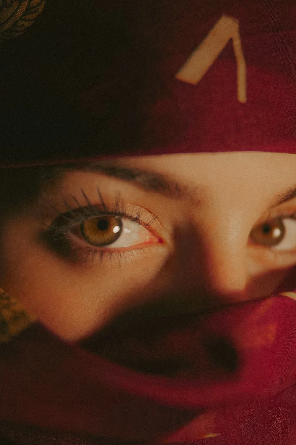 Zoom sur un visage de femme, avec un seul œil visible, portant un turban ou foulard rouge.