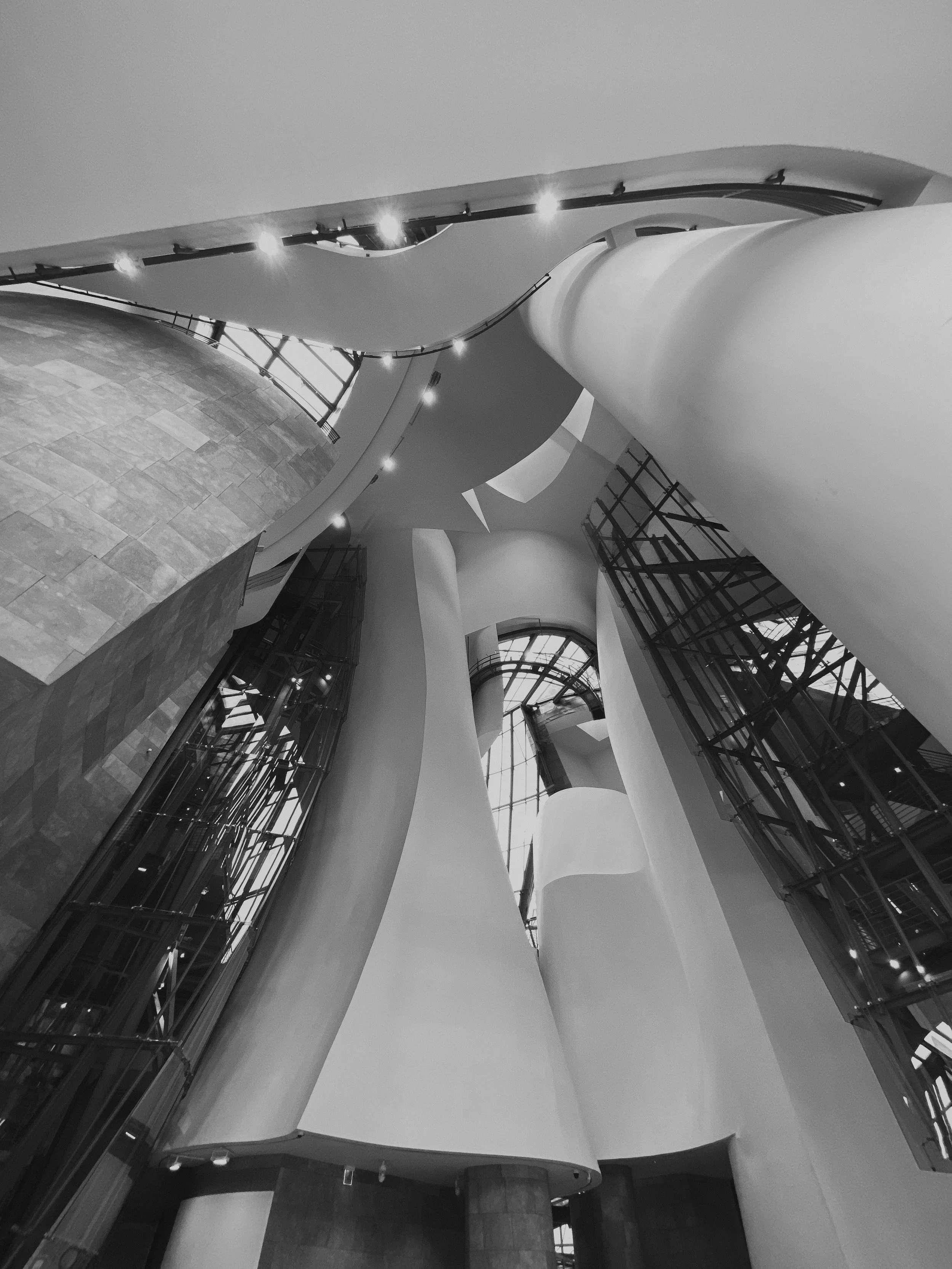 Vue en plongée d'une architecture moderne avec des énormes colonnes courbées, des murs en verre et un ciel visible par de grandes fenêtres.