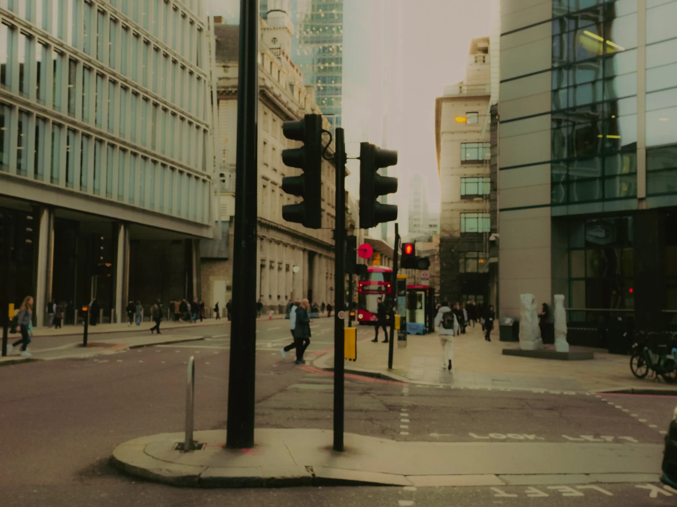 Une intersection en milieu urbain avec des feux de circulation, des passants et des bâtiments modernes en arrière-plan.