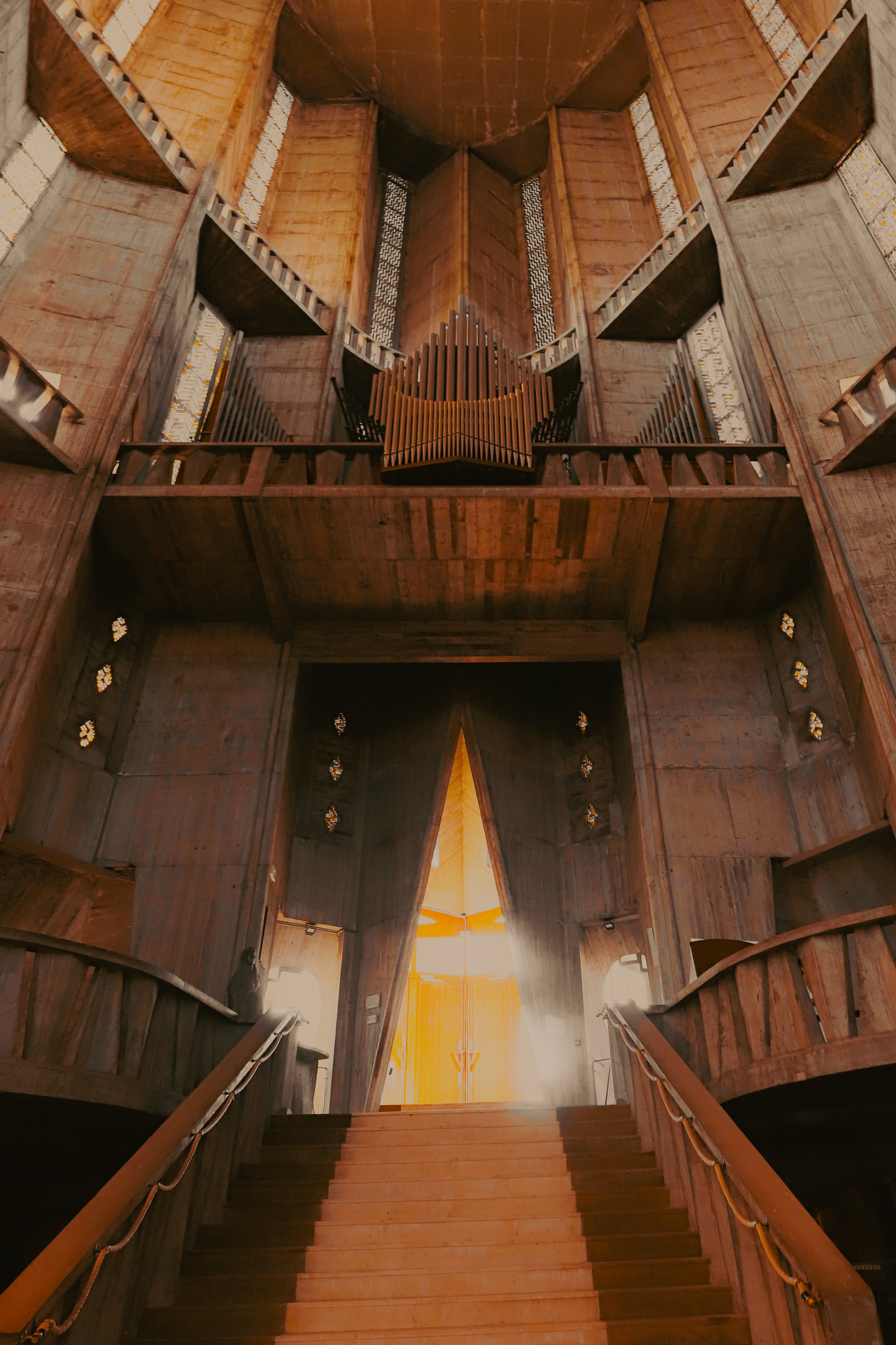 Vue intérieure d'une grande église ou cathédrale en bois avec une grande porte au fond, un escalier menant à l'entrée, et un orgue en haut.