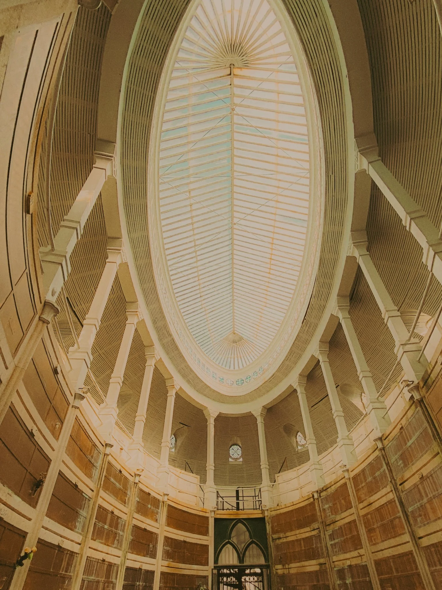 Vue intérieure d'une bibliothèque ou d'une salle de lecture avec un plafond ovale en verre, murs tapissés de livres et balcons en étage.