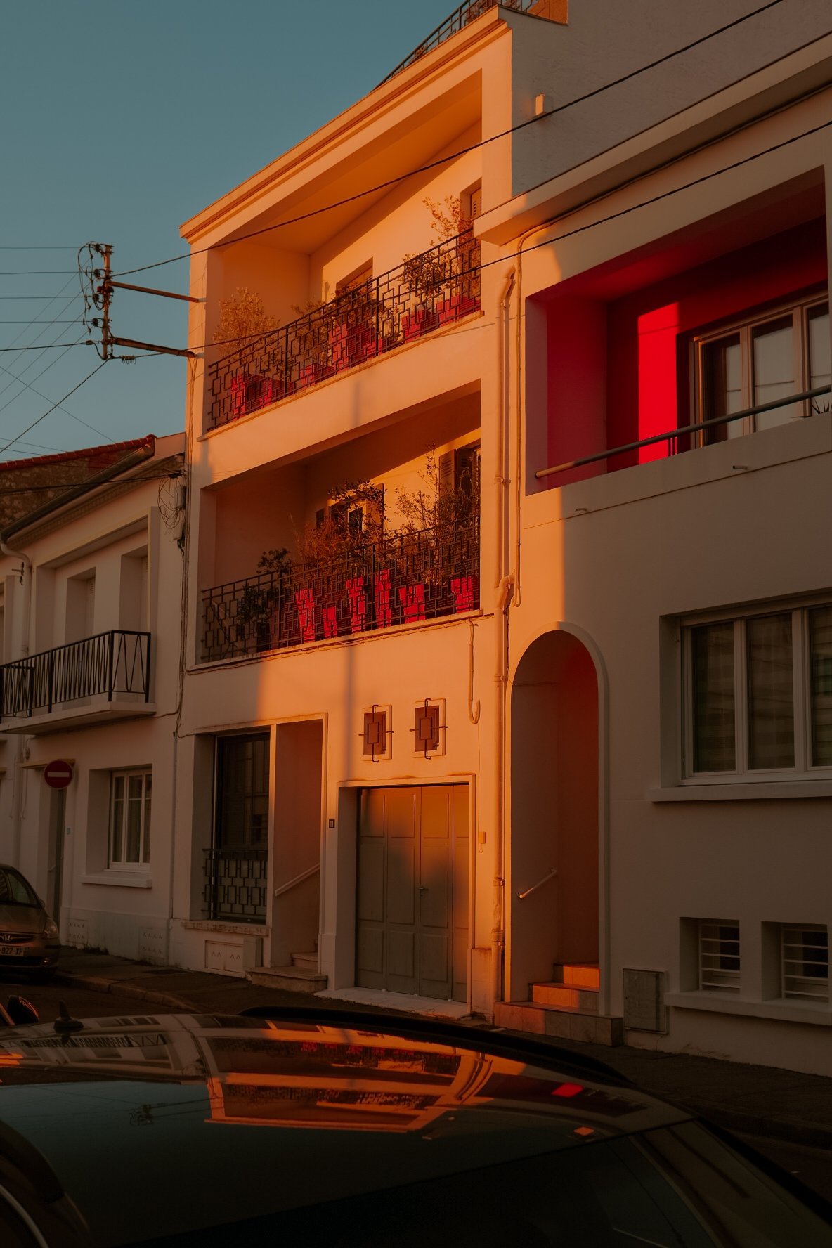 Le coucher du soleil illumine une façade d'immeuble blanc avec des balcons en fer forgé, créant une ambiance chaleureuse avec des teintes orangées et rouges.