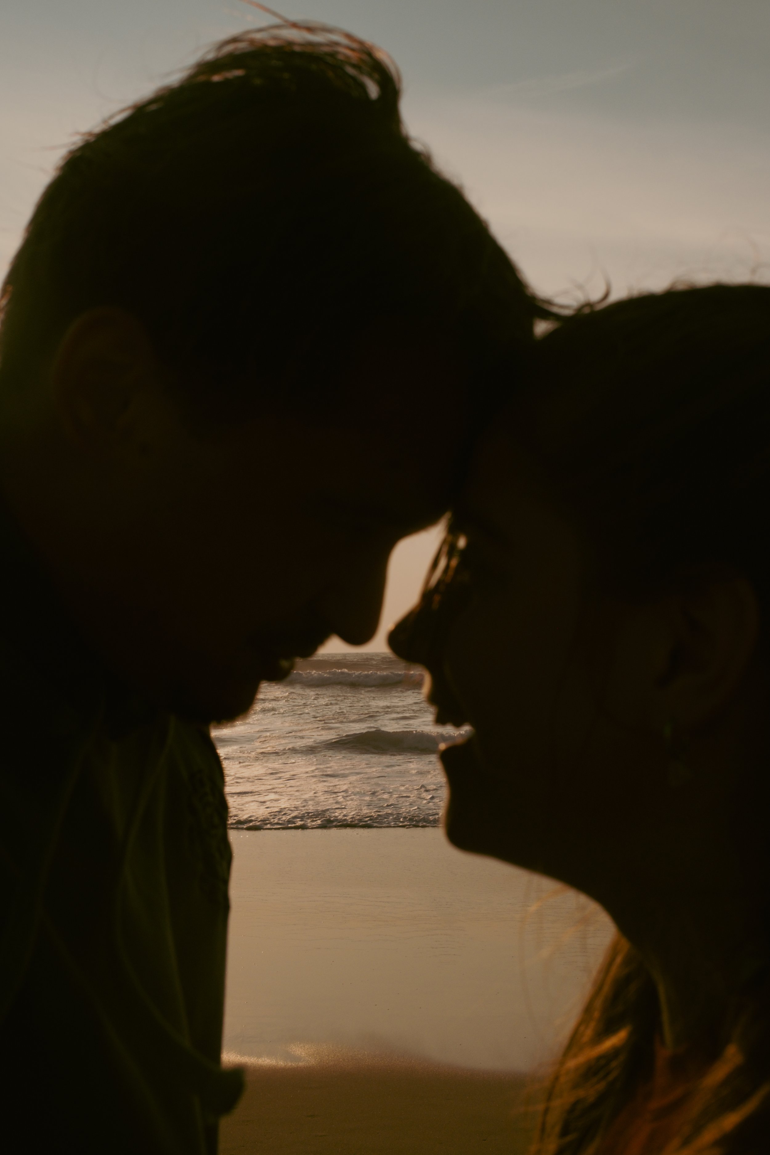 Un couple en silhouette sur la plage au coucher du soleil, se regardant proche du visage.