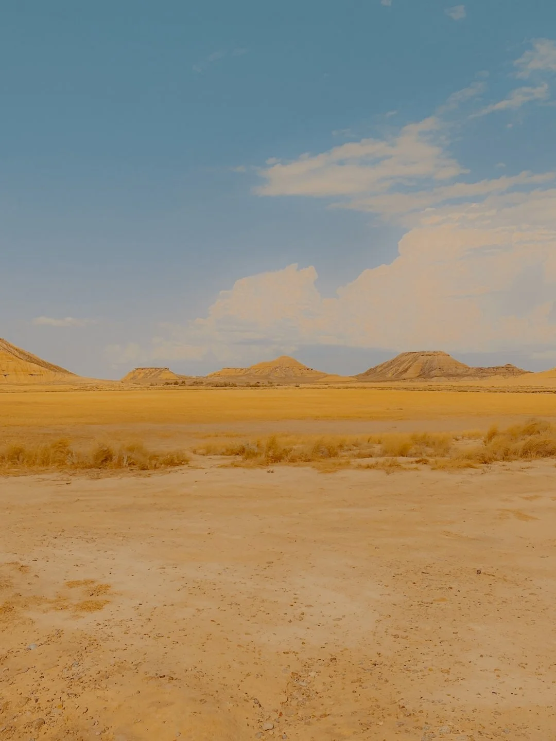 Paysage désertique avec des collines rocheuses sous un ciel bleu avec quelques nuages.