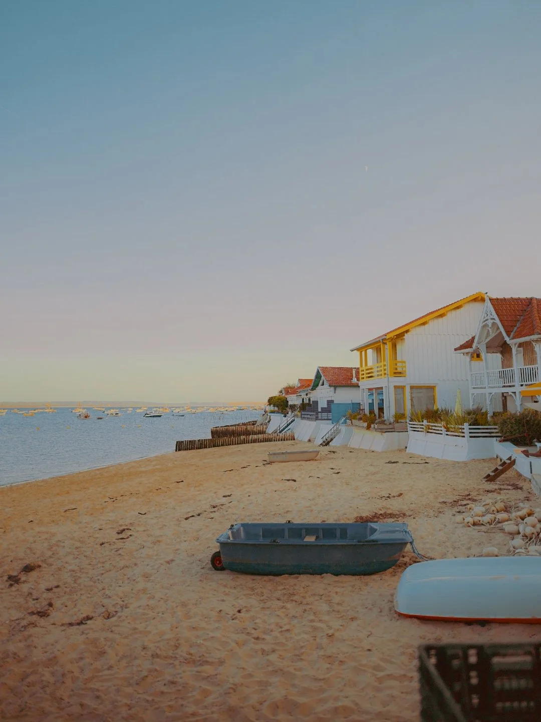 Plage avec sable, petites embarcations, maisons colorées en bord de mer, ciel clair.