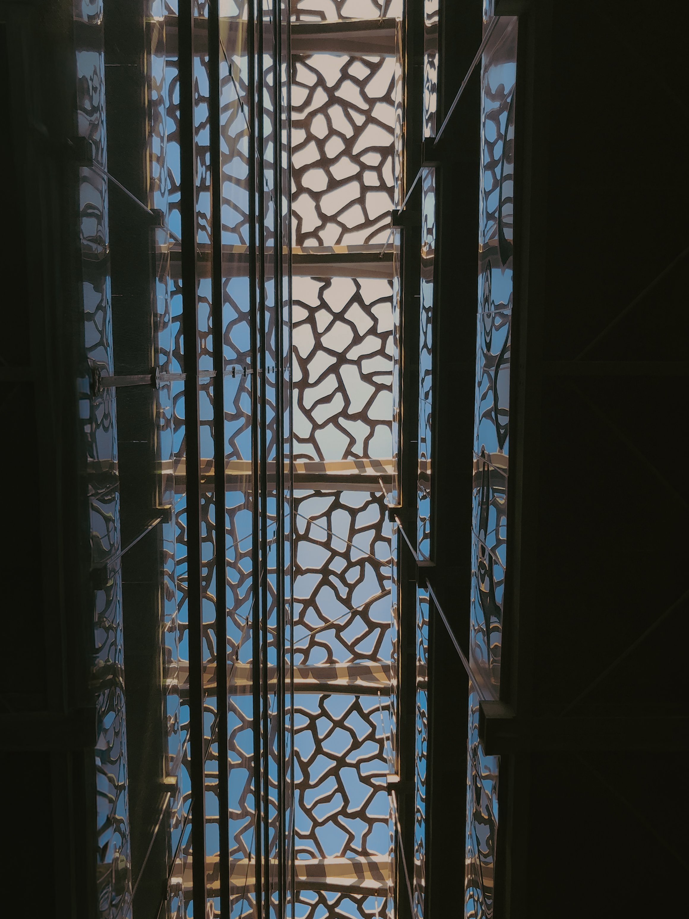 Vue du plafond avec un motif de grille en forme de réseau abstrait, laissant passer la lumière bleue en arrière-plan.