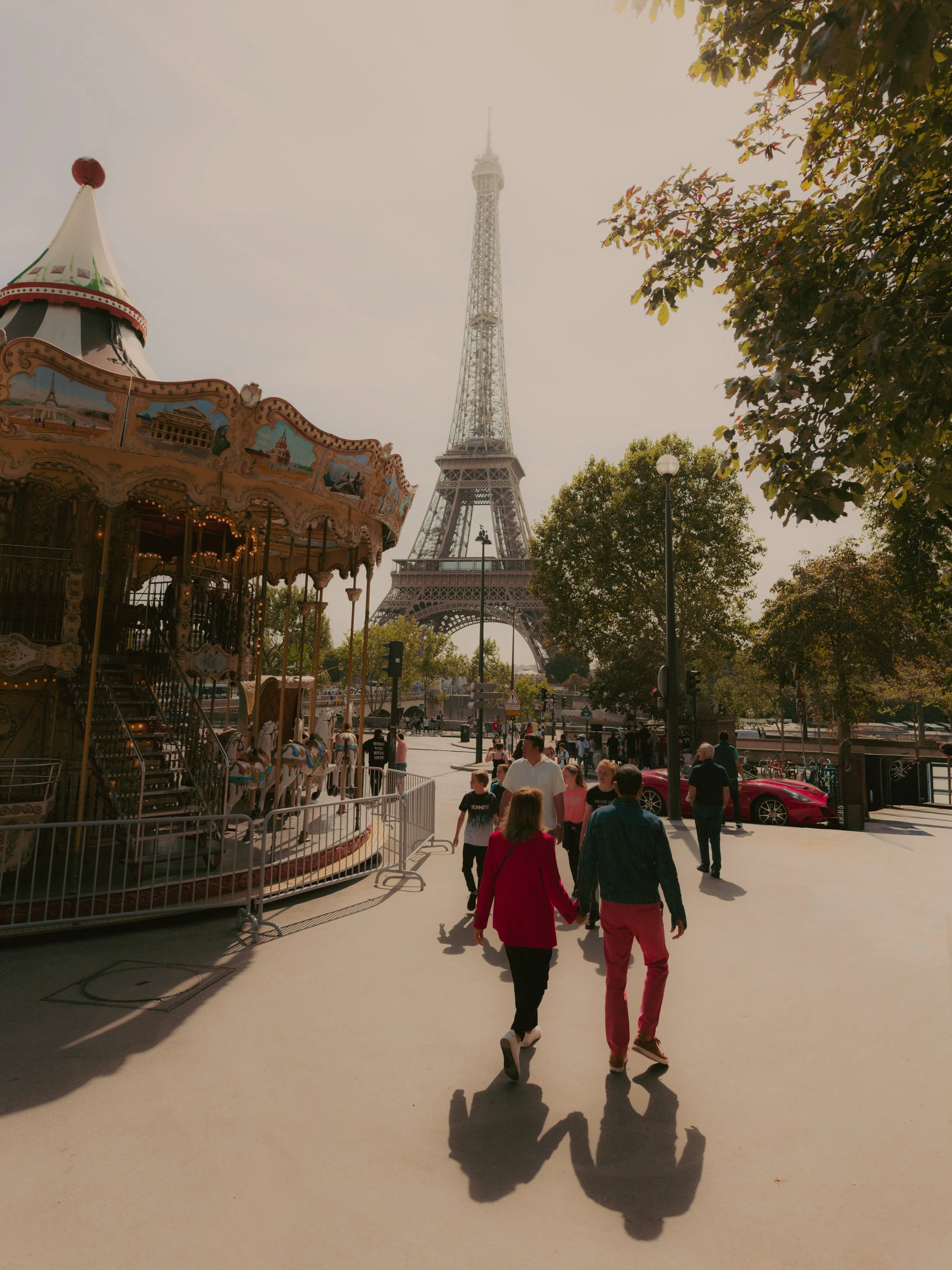 Famille marchant dans une avenue près de la Tour Eiffel à Paris, avec une grande roue et des manèges dans le parc d'attractions à gauche.