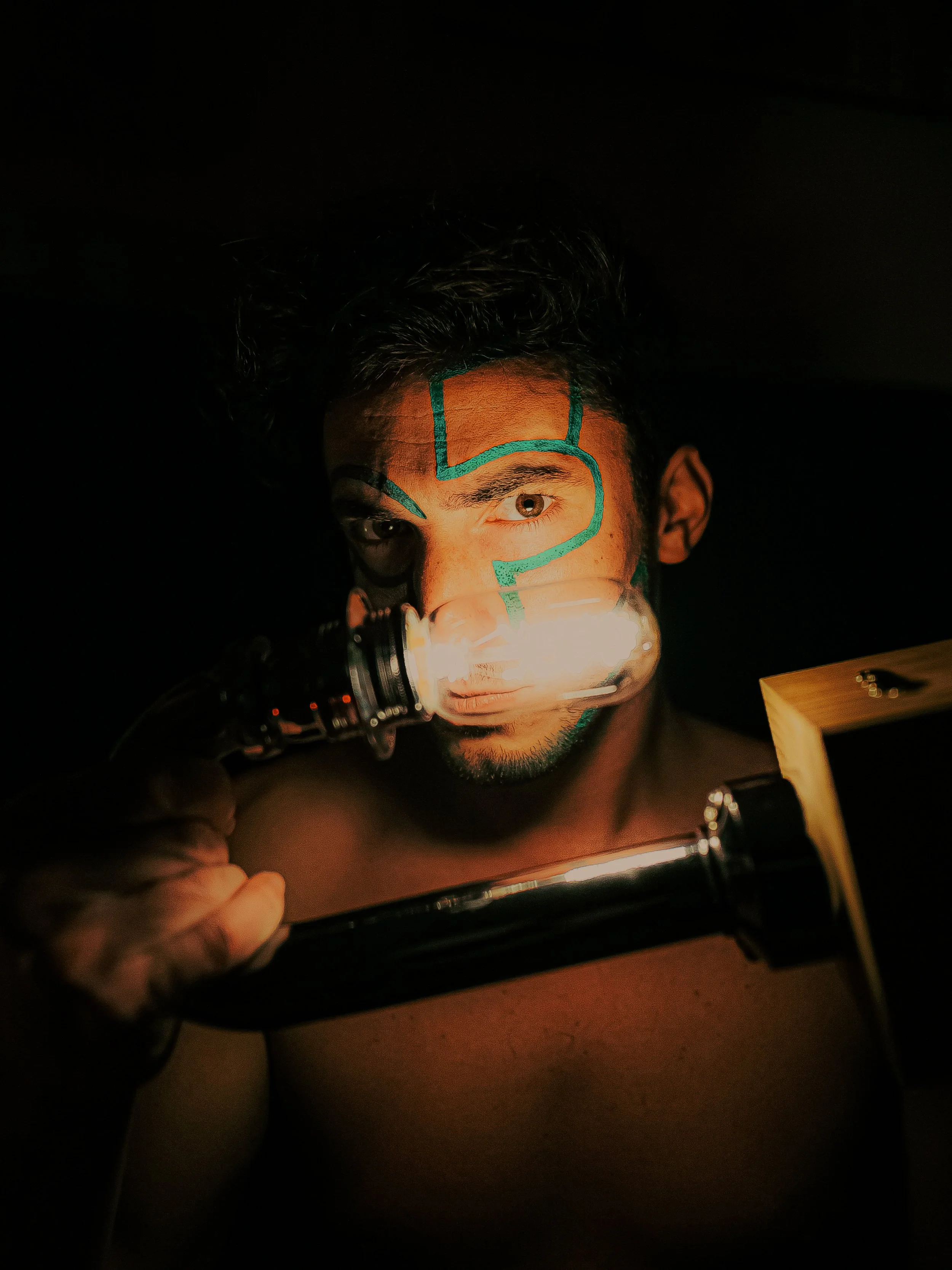 Un homme regarde à travers une lampe de poche, avec des dessins en bleu sur son visage.