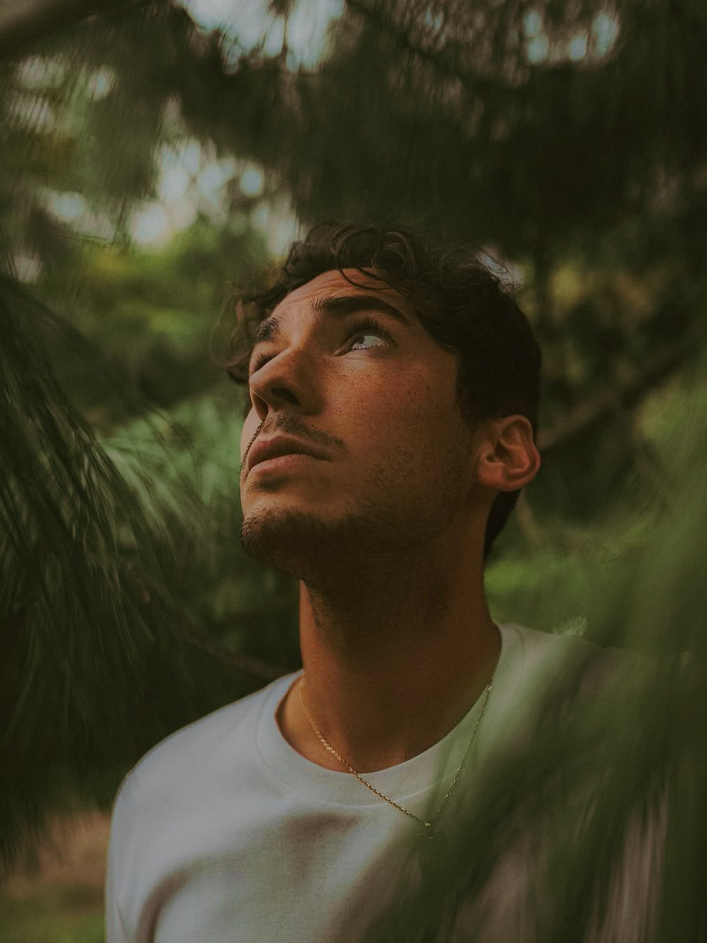 Un jeune homme écoute attentivement, entouré de verdure et d'arbres.