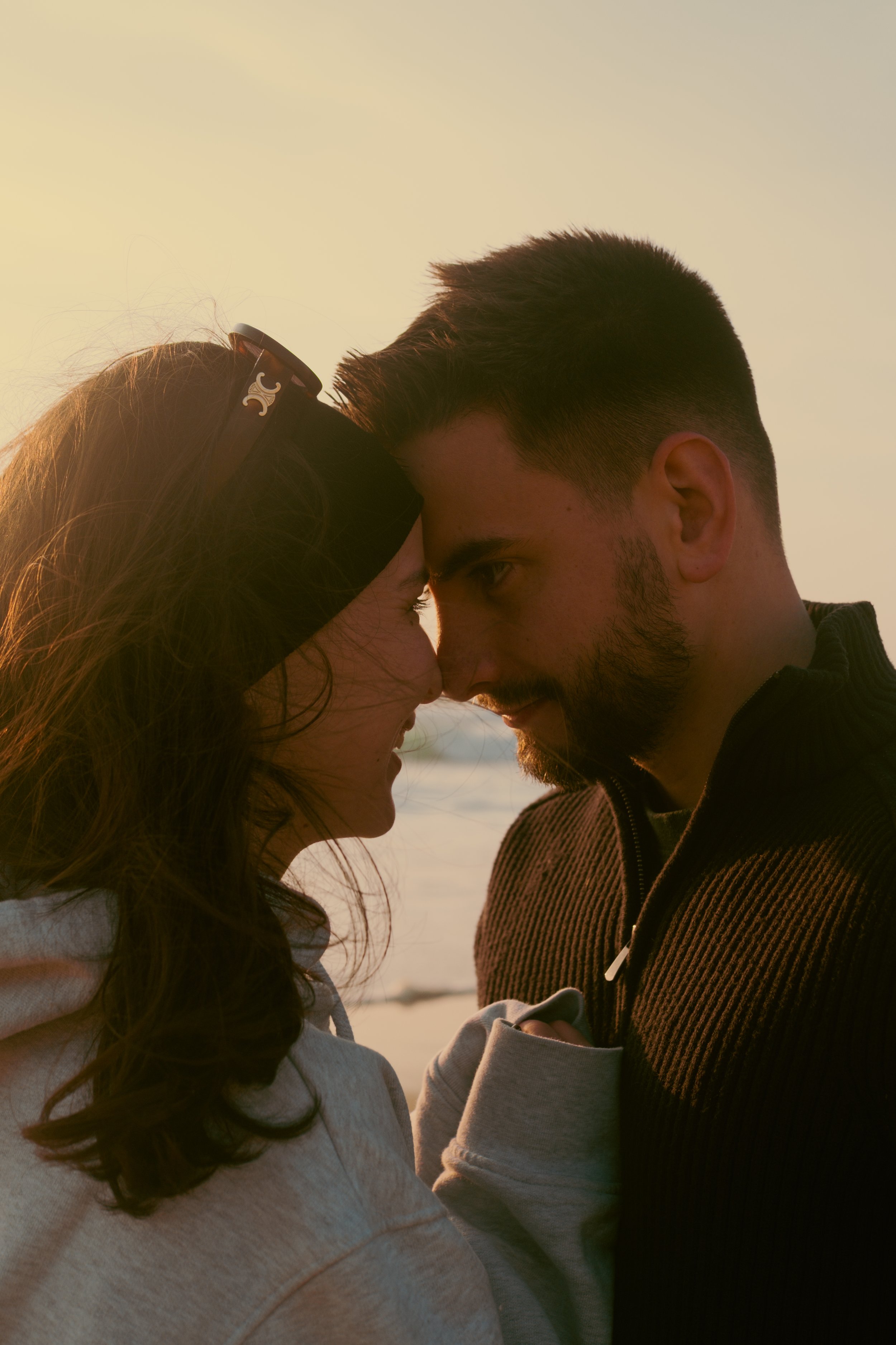 Un couple qui se regarde tendrement avec le front contre front, avec le coucher de soleil en arrière-plan.